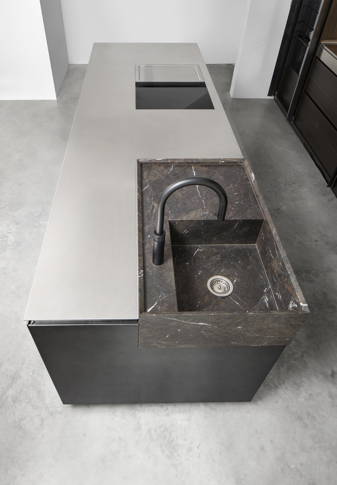 Modern kitchen island with a marble sink and a black faucet, including a built-in stovetop on a flat, beige countertop.