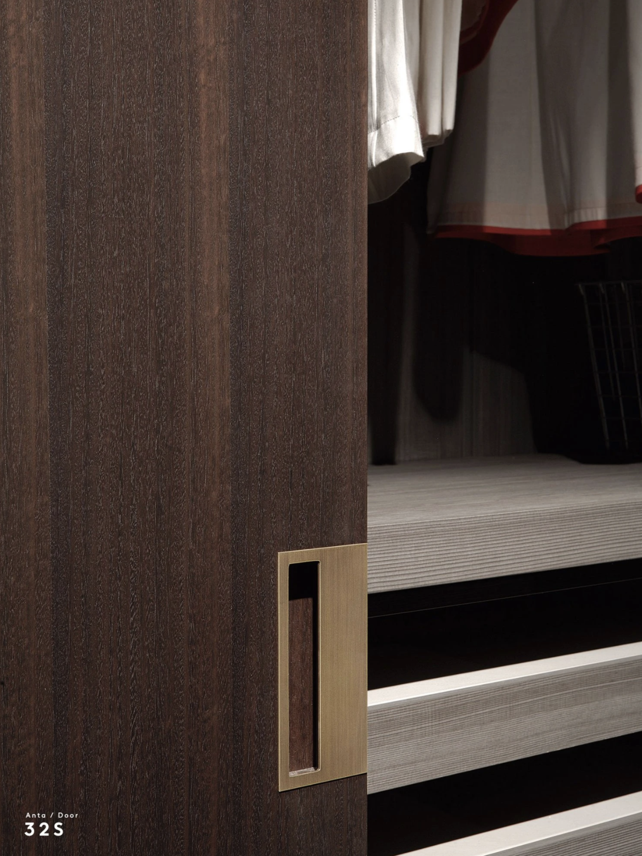 Close-up of a sliding door with a brass handle in a walk-in closet with hanging clothes and wood shelves.