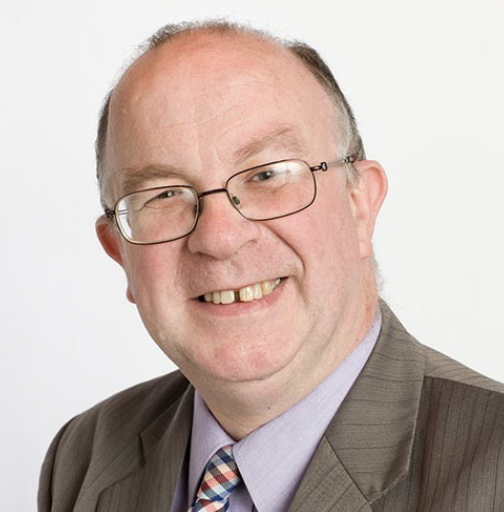 A smiling middle-aged man with glasses, wearing a suit and tie, on a white background.