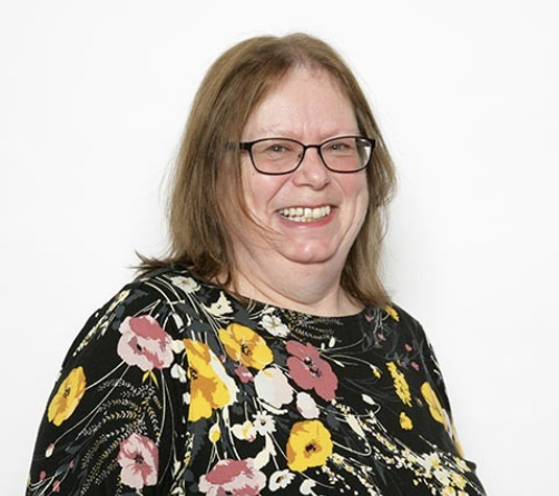 Woman with glasses smiling, wearing a black floral dress with pink, yellow, and white flowers.