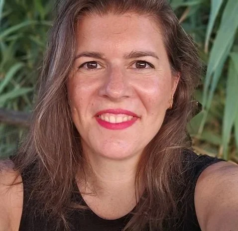 A AI innovation leader woman with long brown hair smiling in front of green plants.