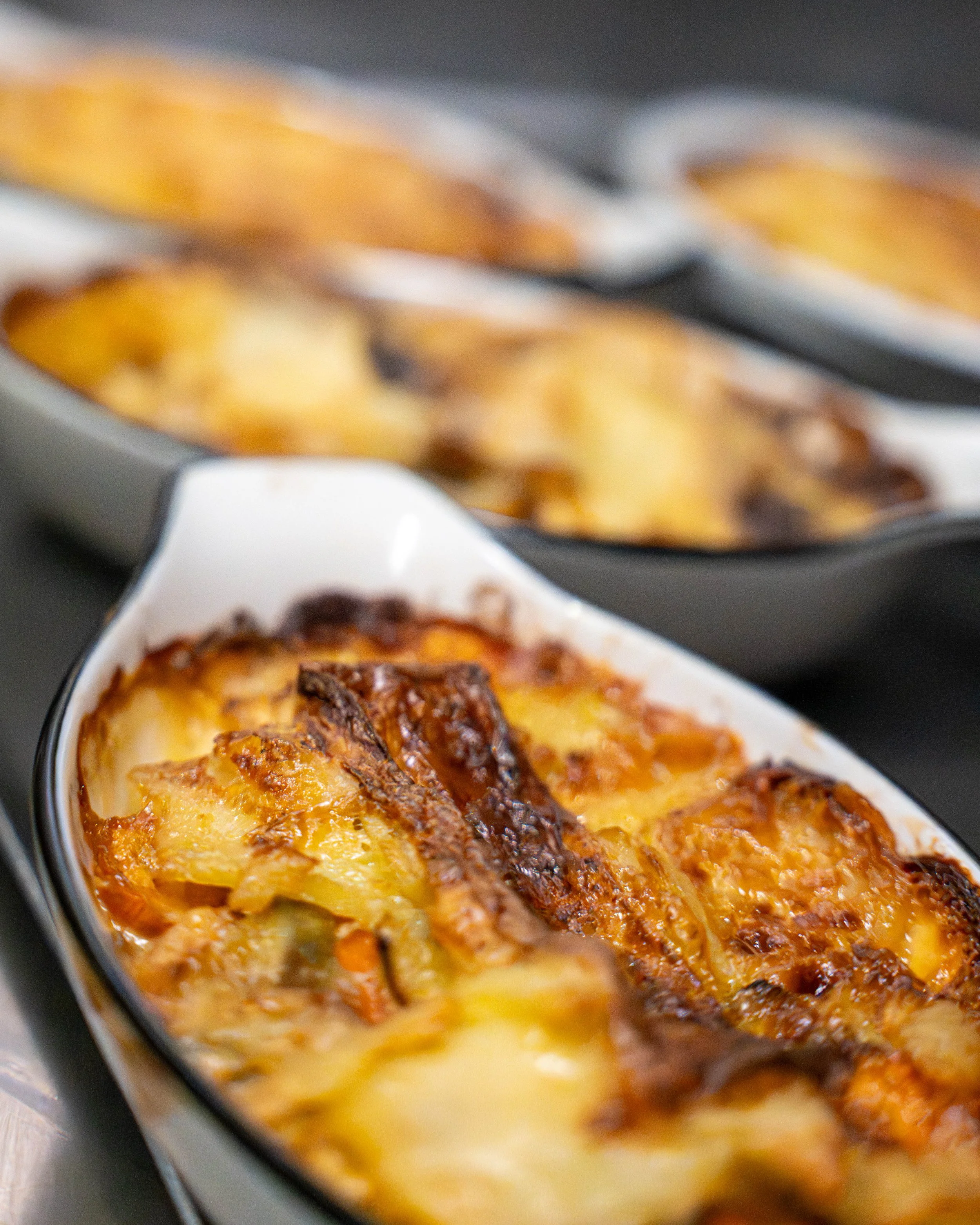 Deux plats de gratin de pommes de terre avec du fromage fondu et une croûte dorée, présentés dans des plats rectangulaires blancs avec un rebord noir.