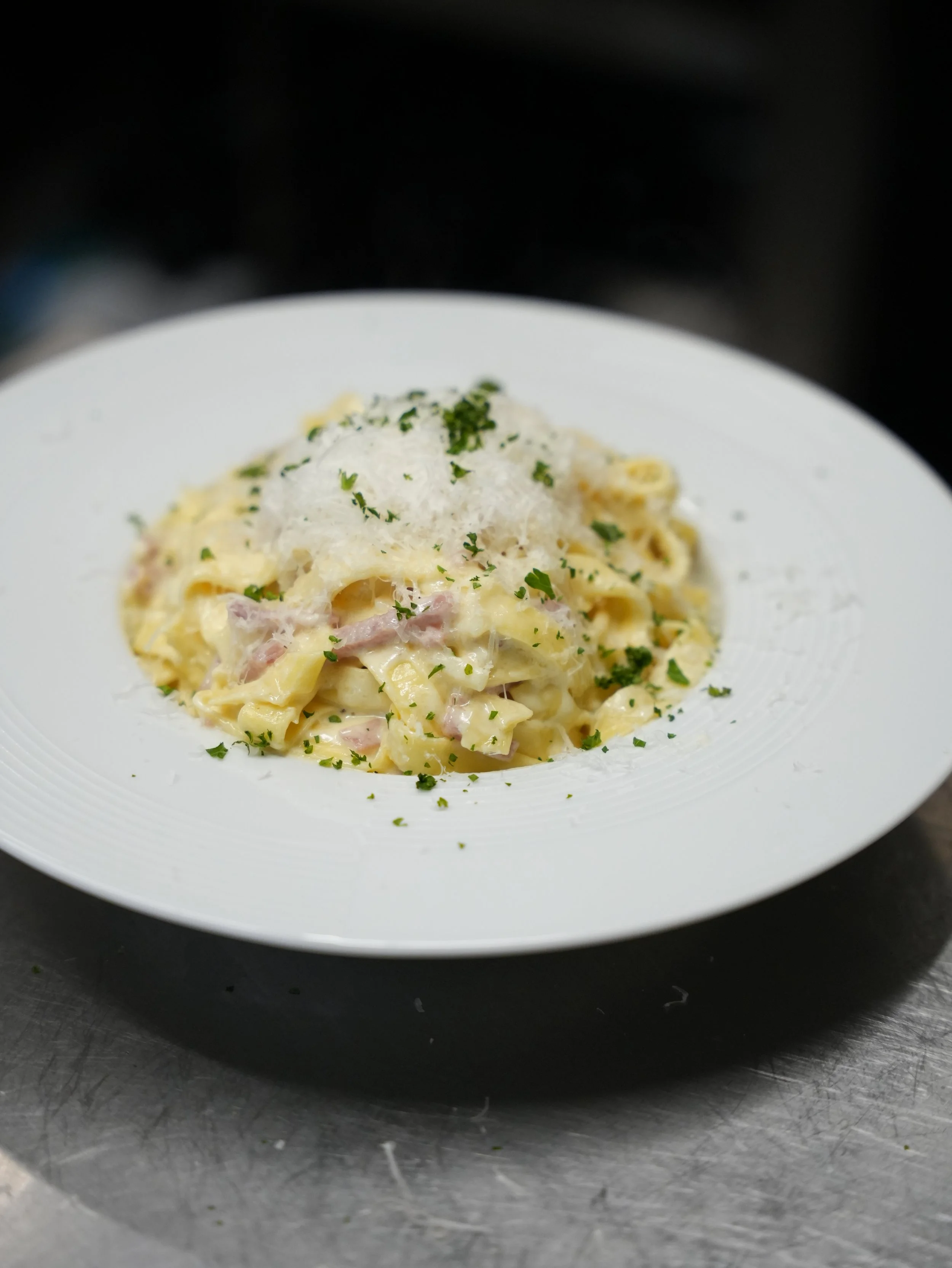 Assiette de pâtes à la crème, avec morceaux de jambon, garnie de fromage et de persil.
