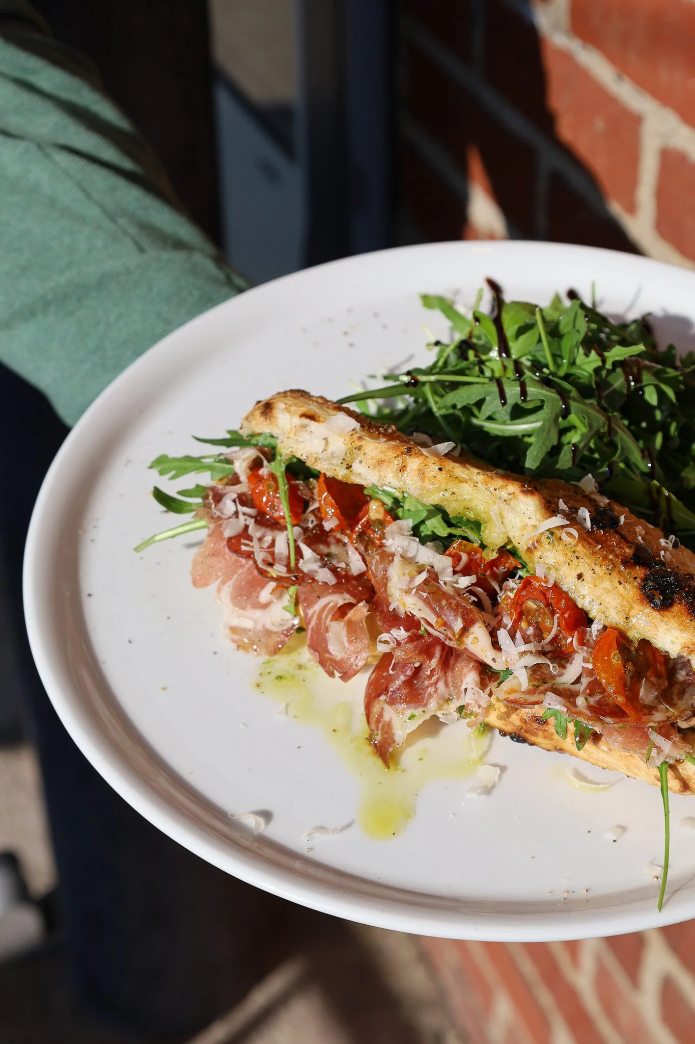 Une assiette avec un sandwich à la viande, une salade verte avec une vinaigrette balsamique, et des tomates cerises, présenté de manière élégante.