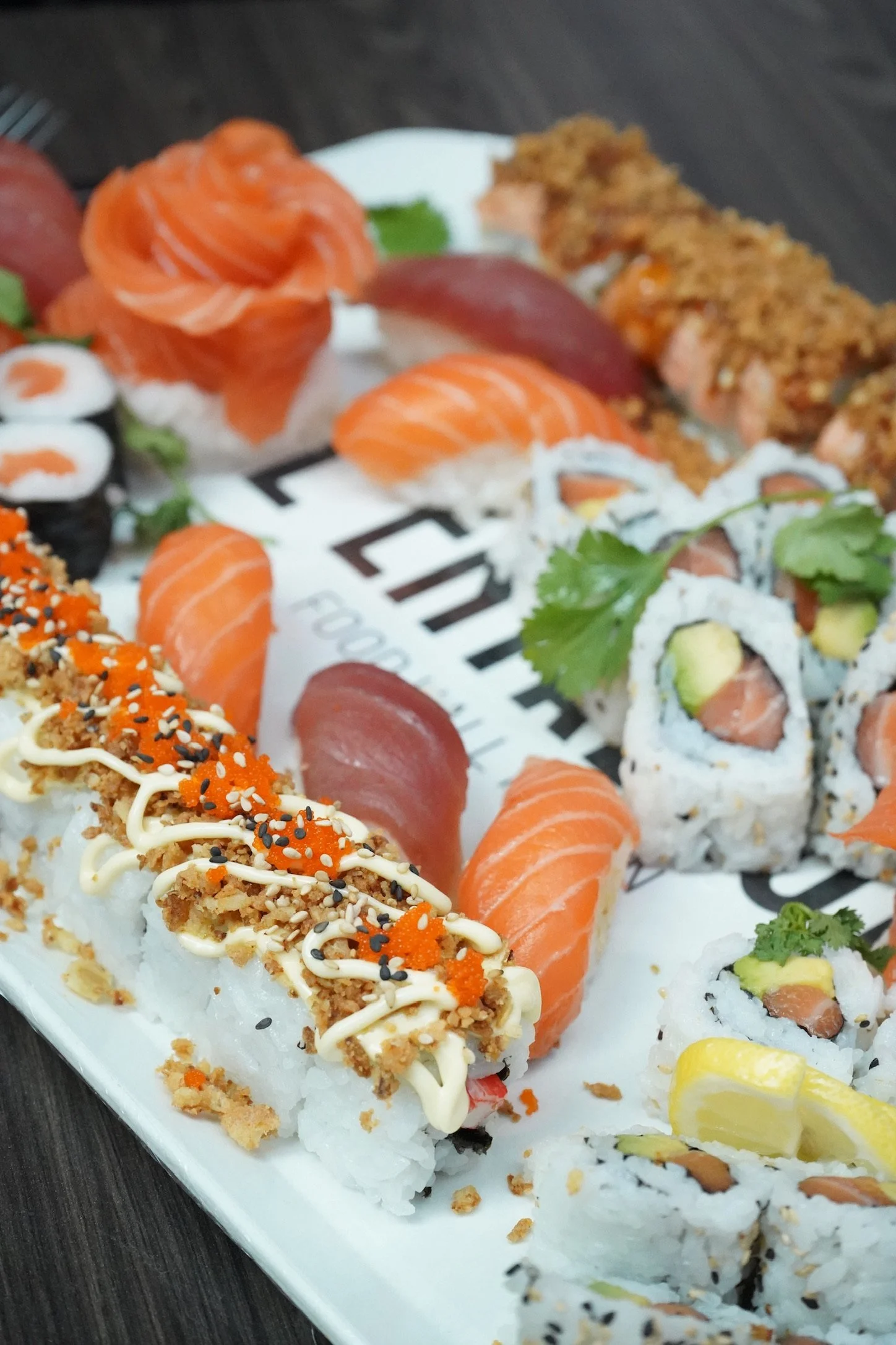 Plate de sushi variés avec rouleaux, sashimis, garnitures de poisson, avocat et sauce.