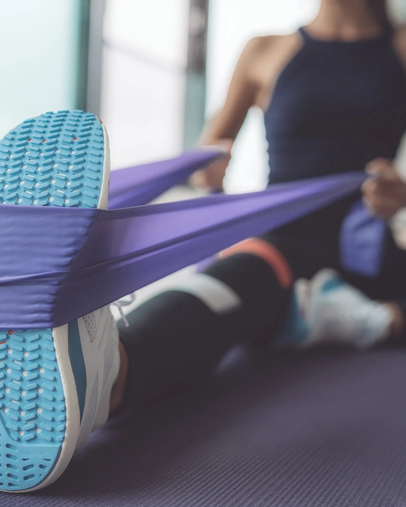 A person holding a purple resistance band while stretching, wearing black athletic clothing and sneakers.