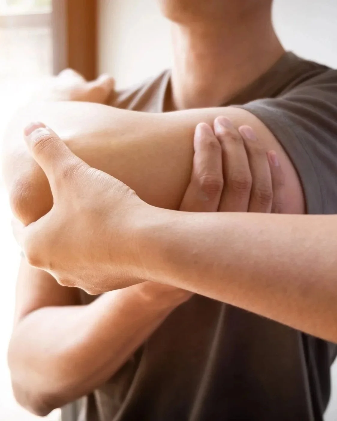 Close-up of a person holding their shoulder with both hands, stretching or massaging it.
