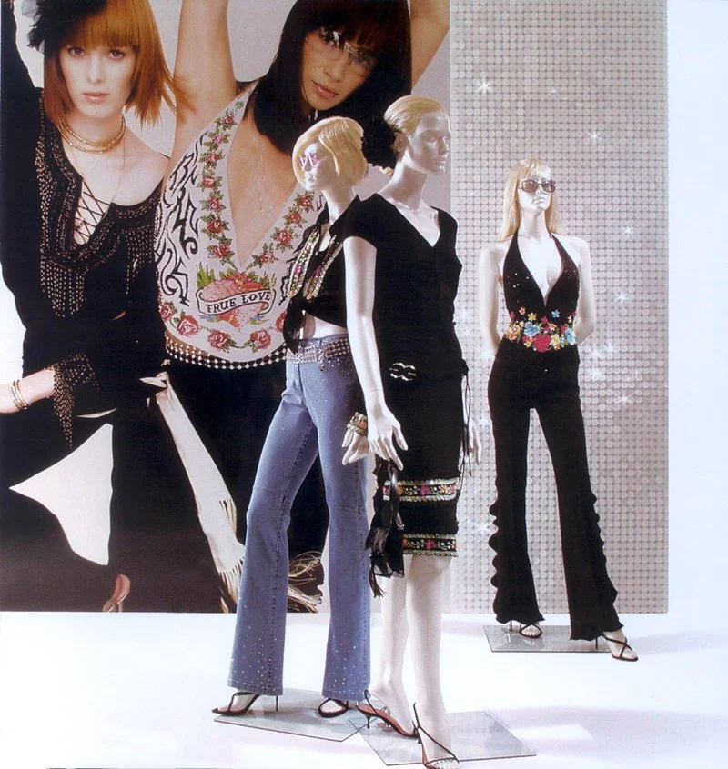 Drei Mode-Mannequins in schwarzen Outfits mit bunten Stickereien, in einer Modenschau-Ausstellung.