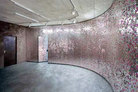 Rund um eine halbkreisförmige Wand sind kleine, reflektierende Mosaikfliesen in einem Raum.