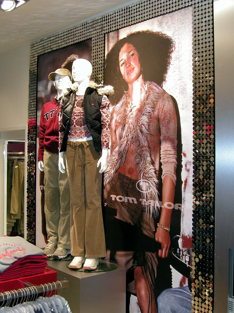 Kindermode mit mannequins, die Kinderkleidung zeigen, und ein großes Poster mit einer Frau, die braune, lockige Haare trägt.