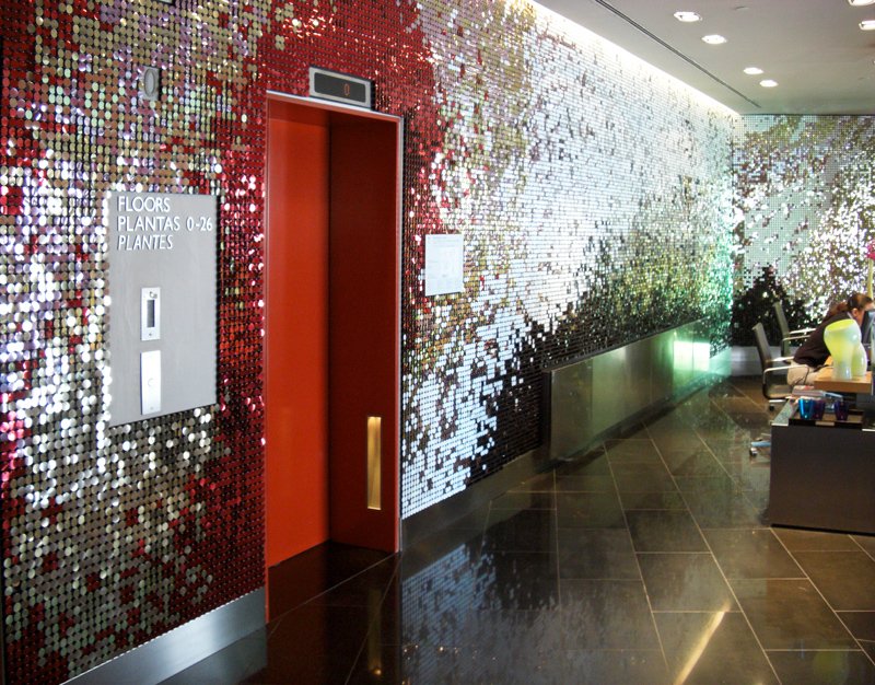 Fahrstuhl in einem modernen, dekorativen Flur mit einer Wand aus roten und weißen Pailletten und einem Sitzbereich mit Personen.