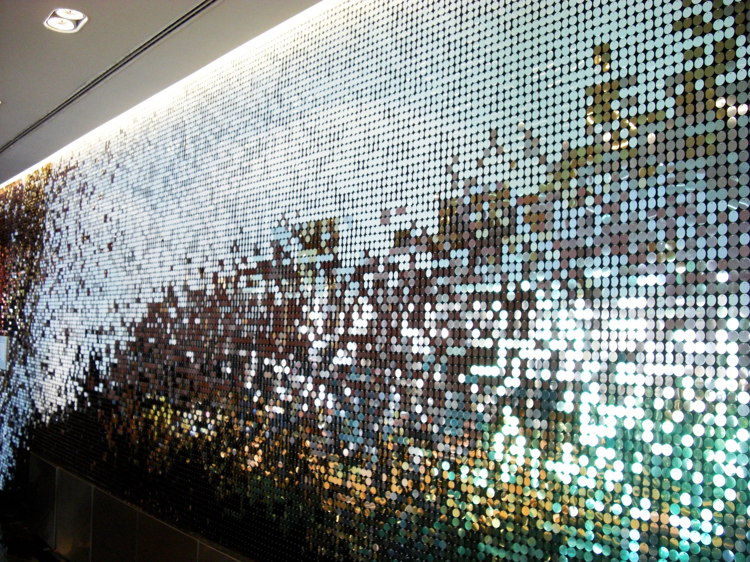 Eine Wanddekoration bestehend aus kleinen, rundlichen, reflektierenden Scheiben, die Licht und Farben spiegeln, mit einer Stadt- oder Naturkulisse im Hintergrund.