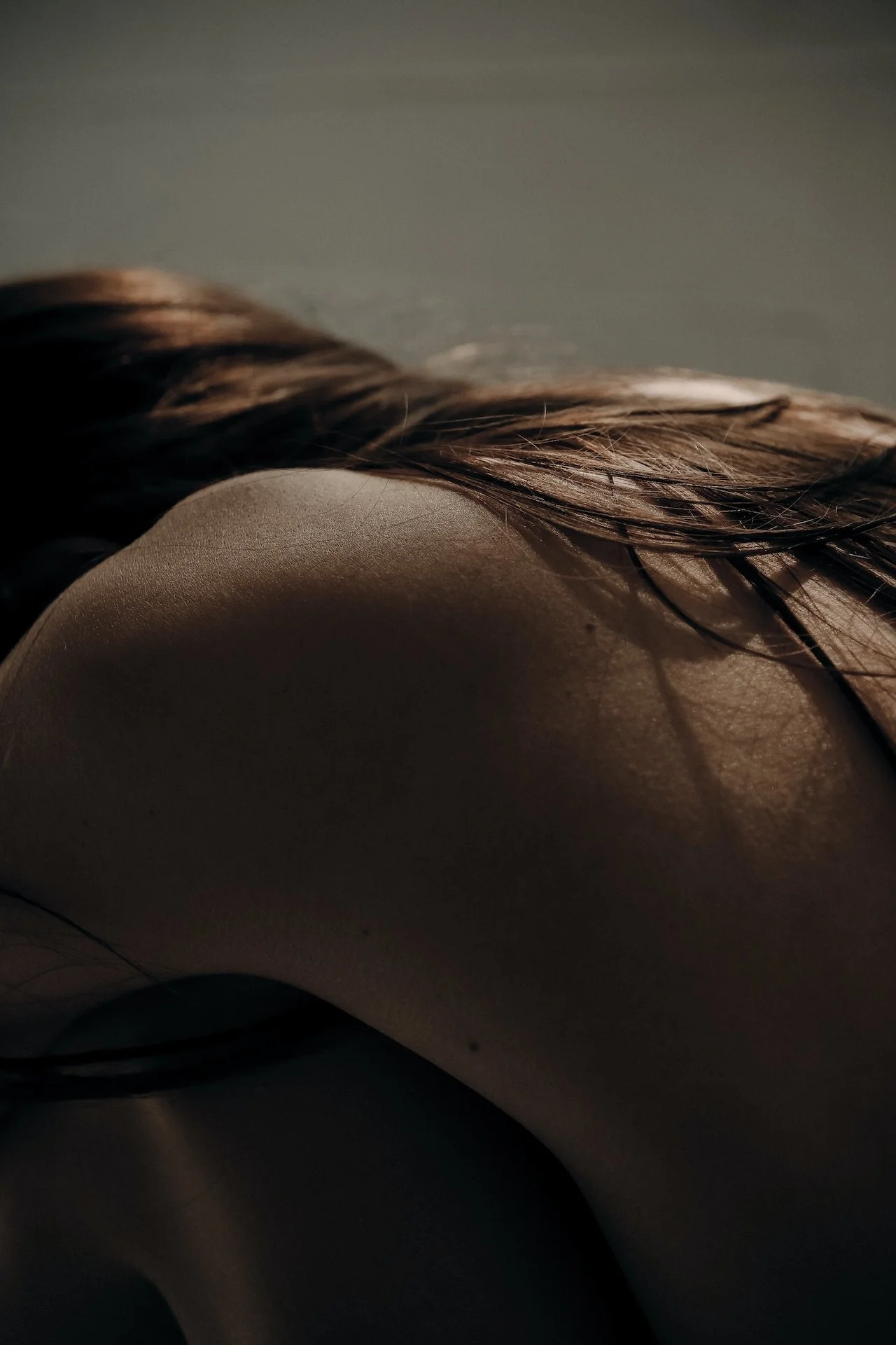 Close-up of a person's shoulder and back, with dark hair, in low lighting.