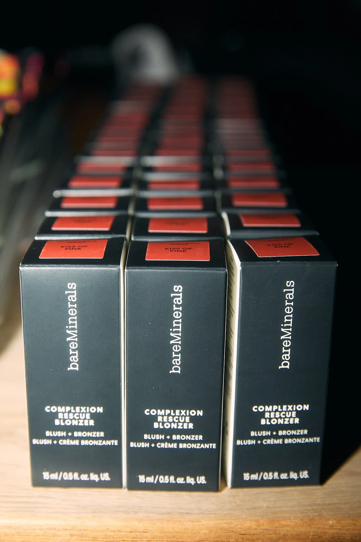Three boxes of bareMinerals Complexion Rescue Blonzer, a blush and bronzer product, placed on a wooden surface.