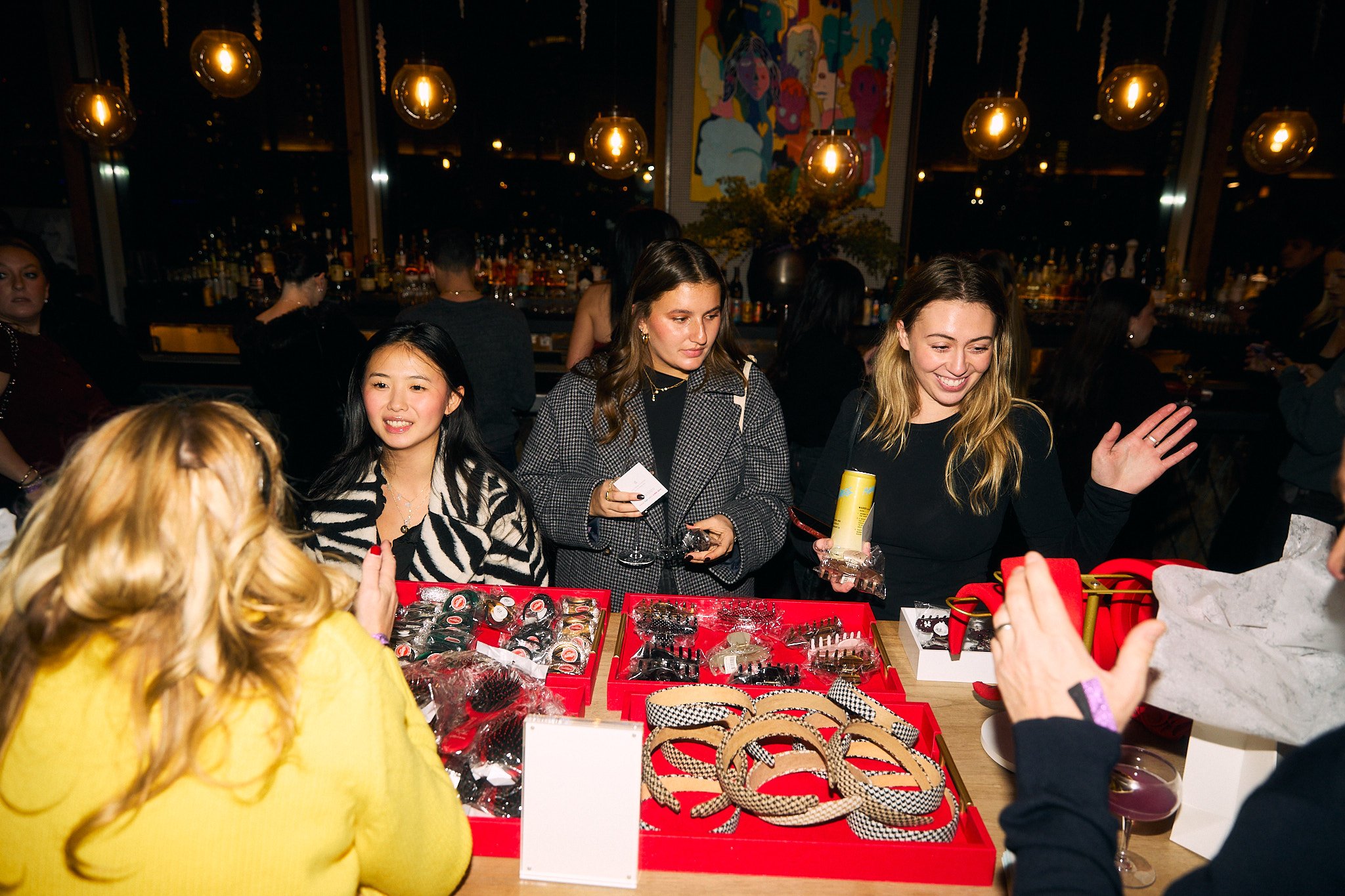 Women shopping for jewelry at a store with a bar in the background and modern lighting overhead.