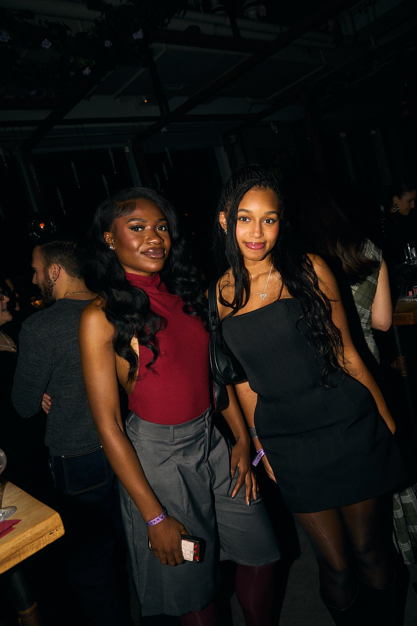 Two women posing for a photo at a social event, with other people in the background.