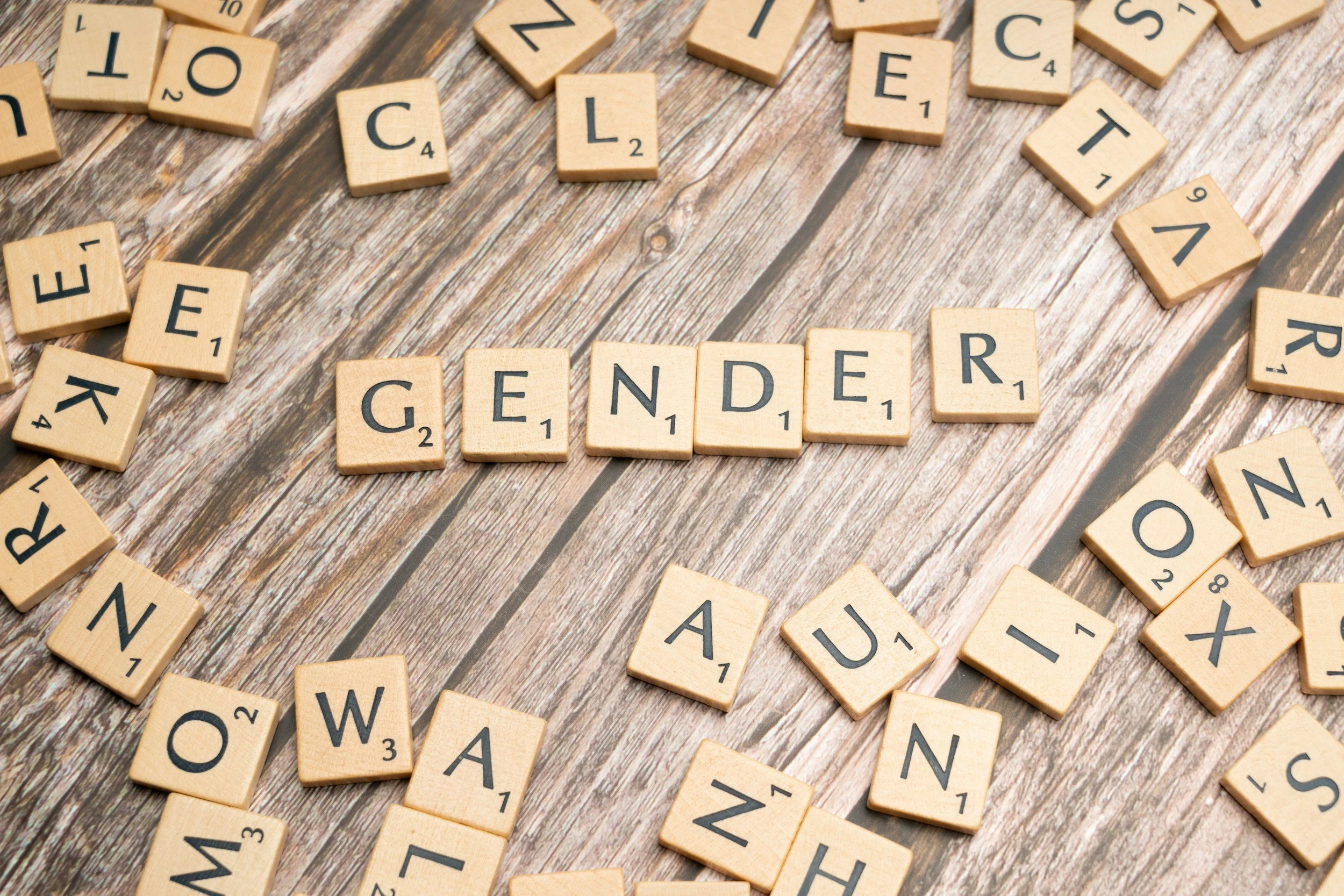 Scrabble tiles spelling the words "GENDER" and "AUN" on a wooden surface.