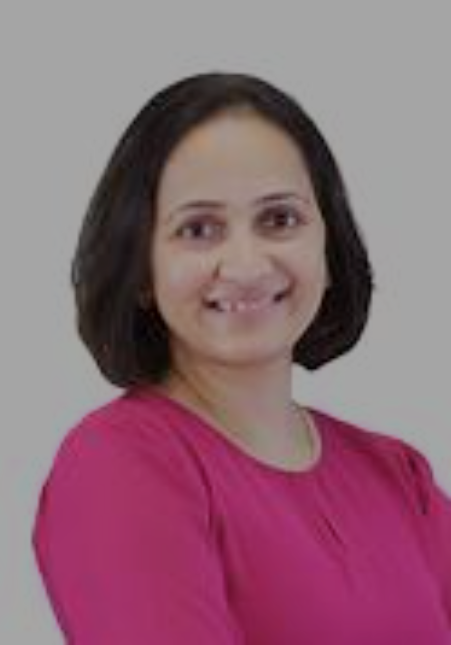 A woman with shoulder-length dark hair wearing a pink top, smiling, in front of a plain gray background.