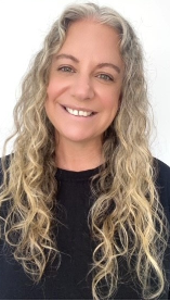Close-up of a smiling woman with curly gray hair, wearing a black top, against a plain white background.