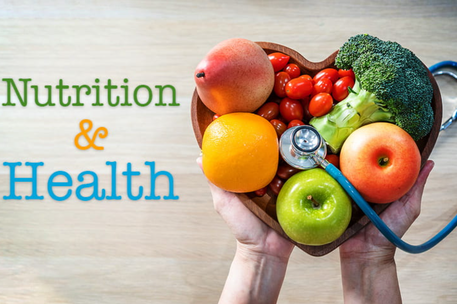 A heart-shaped wooden bowl filled with various fresh fruits and vegetables, with a stethoscope resting on top, and the words 'Nutrition & Health' written on the left side.
