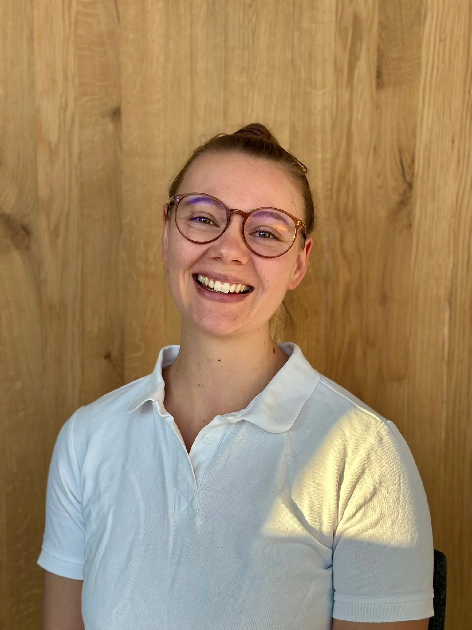 Lächelnde junge Frau mit Brille und weißem Poloshirt.