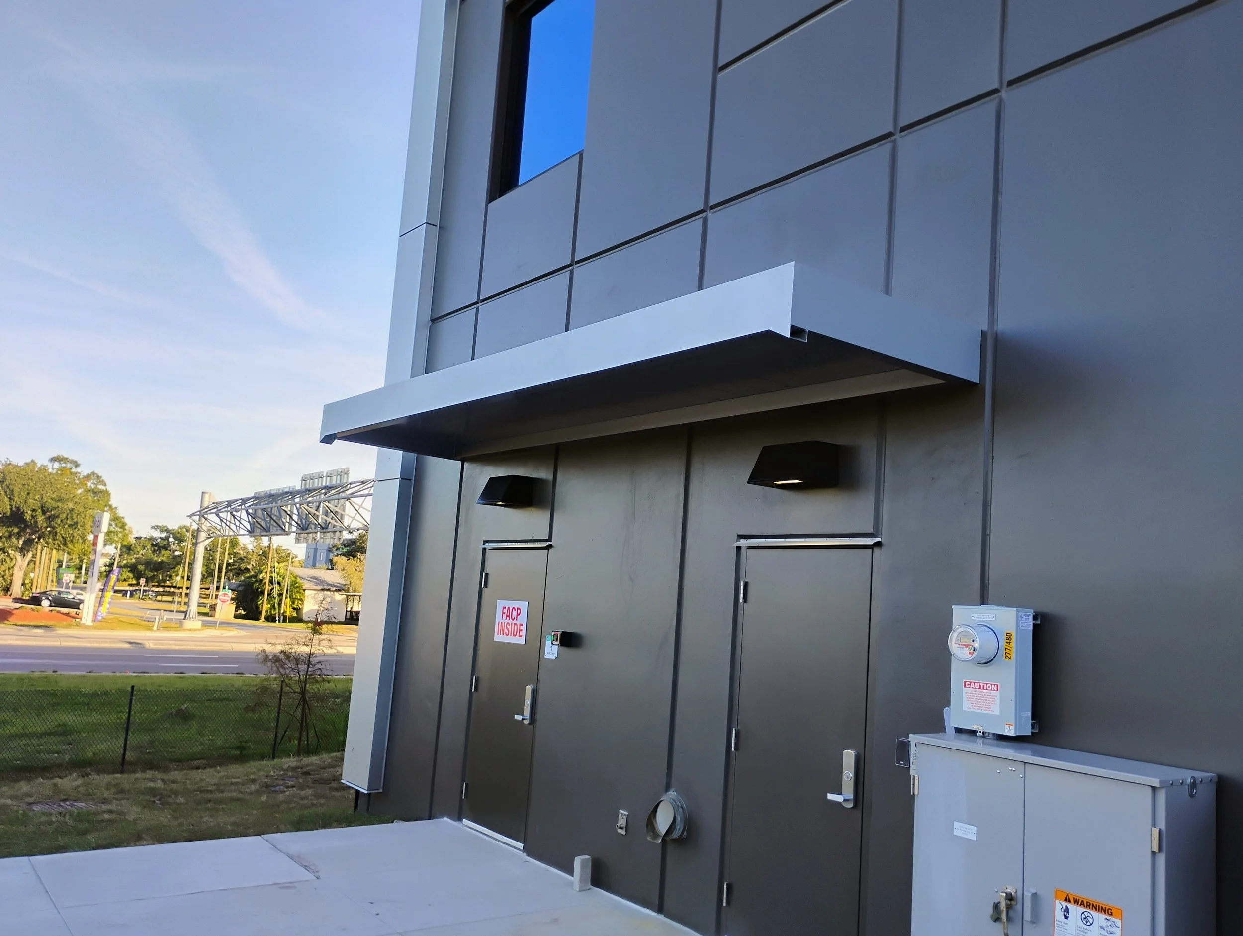 Exterior of a modern building with two black doors covered by a canopie.