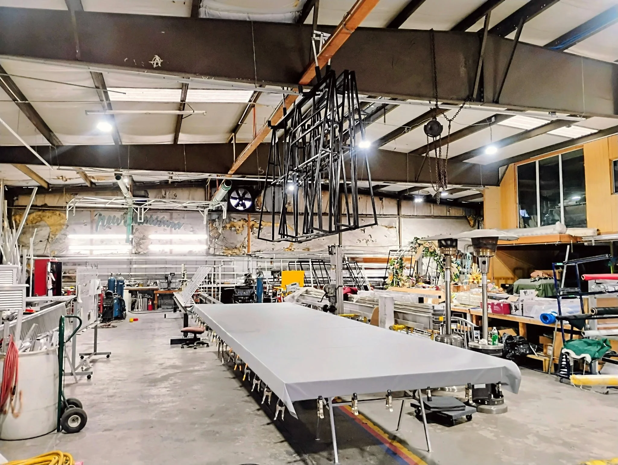 Empty industrial workshop with tables, equipment, and suspended lighting fixtures.