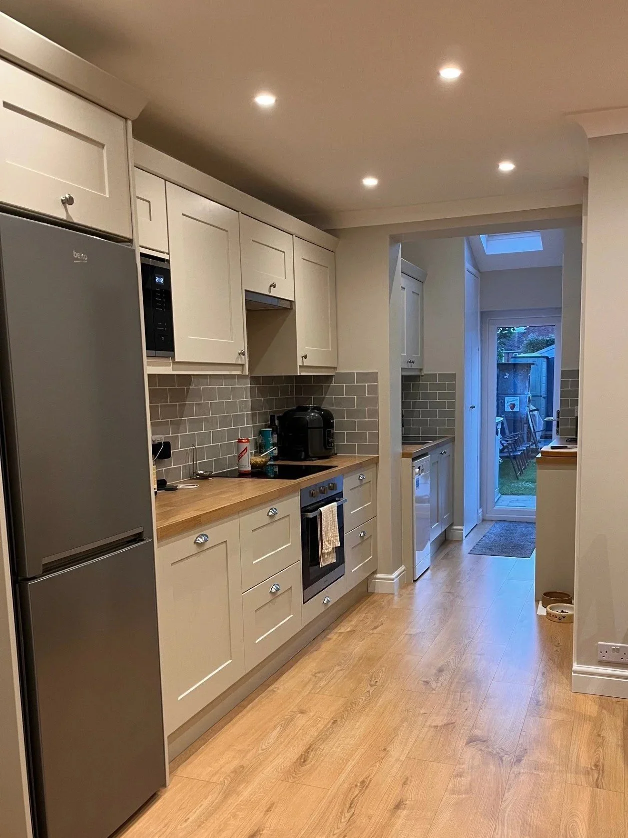 Custom modern shaker kitchen featuring neutral tones and olive green tiles. Renovation included wall removal, plastering, and new spotlights to maximise storage and open-plan living.