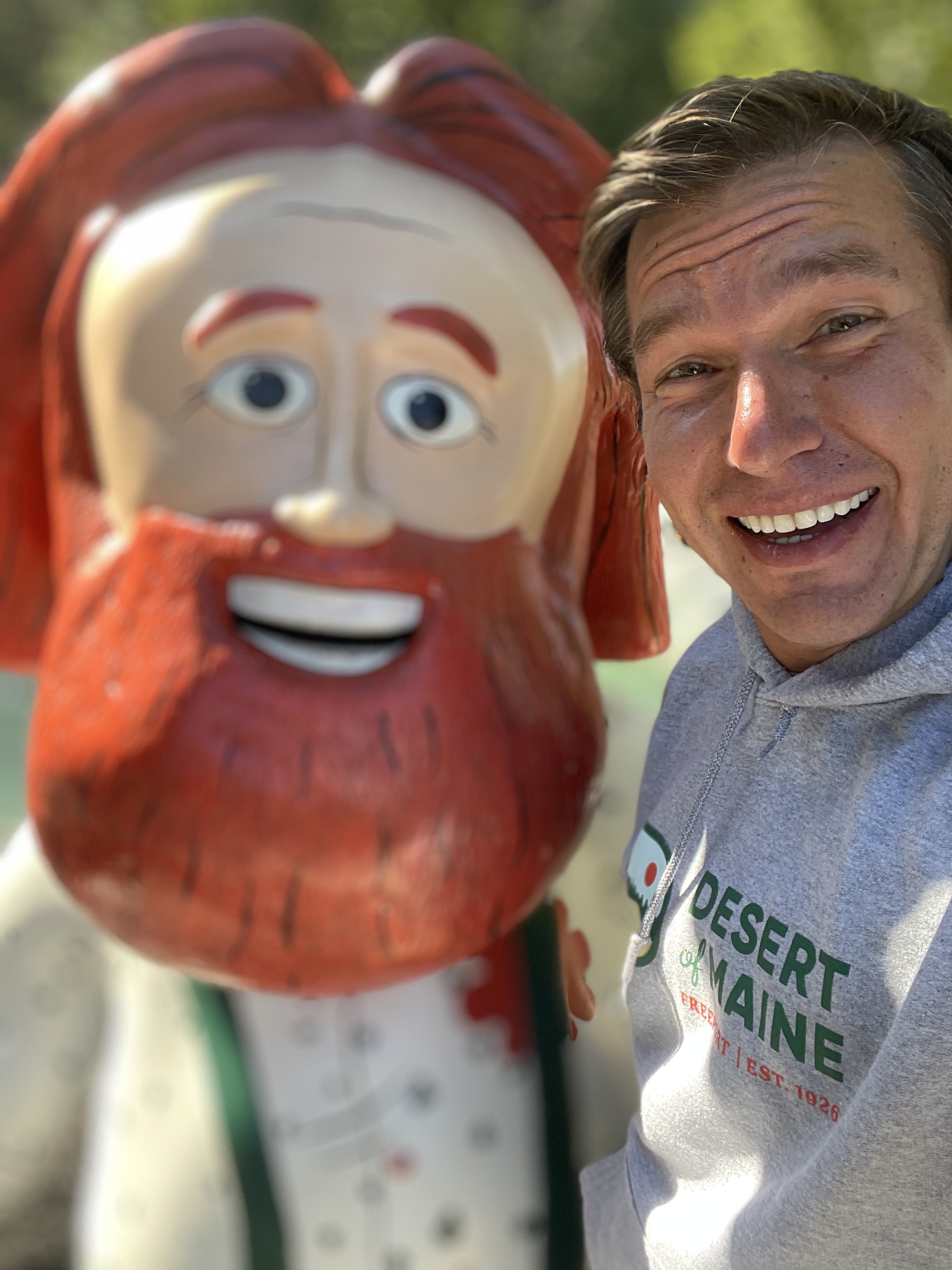 A smiling man, named Julian Schlaver, taking a selfie with a large cartoonish Santa Claus figure outdoors.