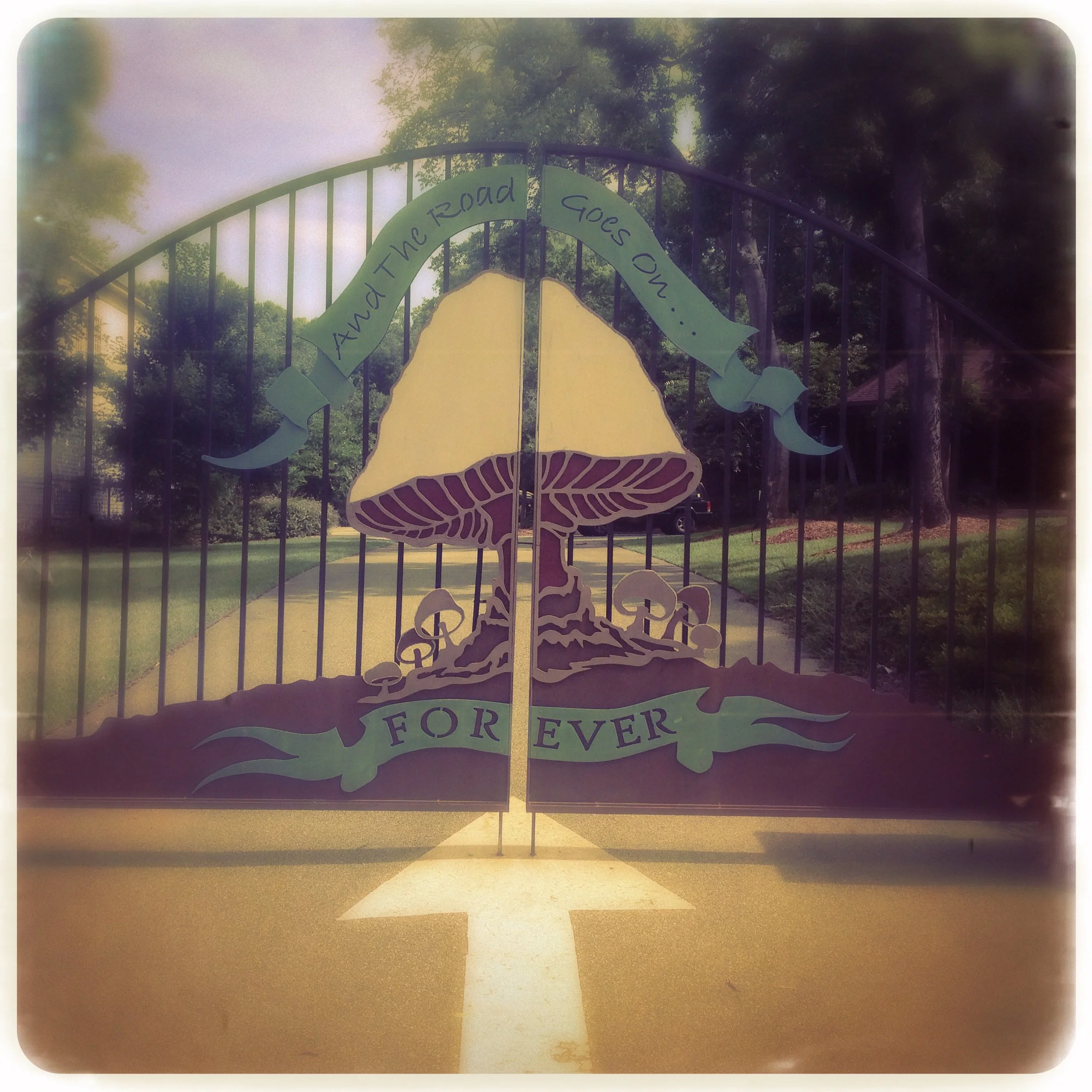 Decorative gate with a large mushroom illustration and the words 'And the road goes on... FOREVER' at the top and bottom, with a road painted on the ground pointing forward.