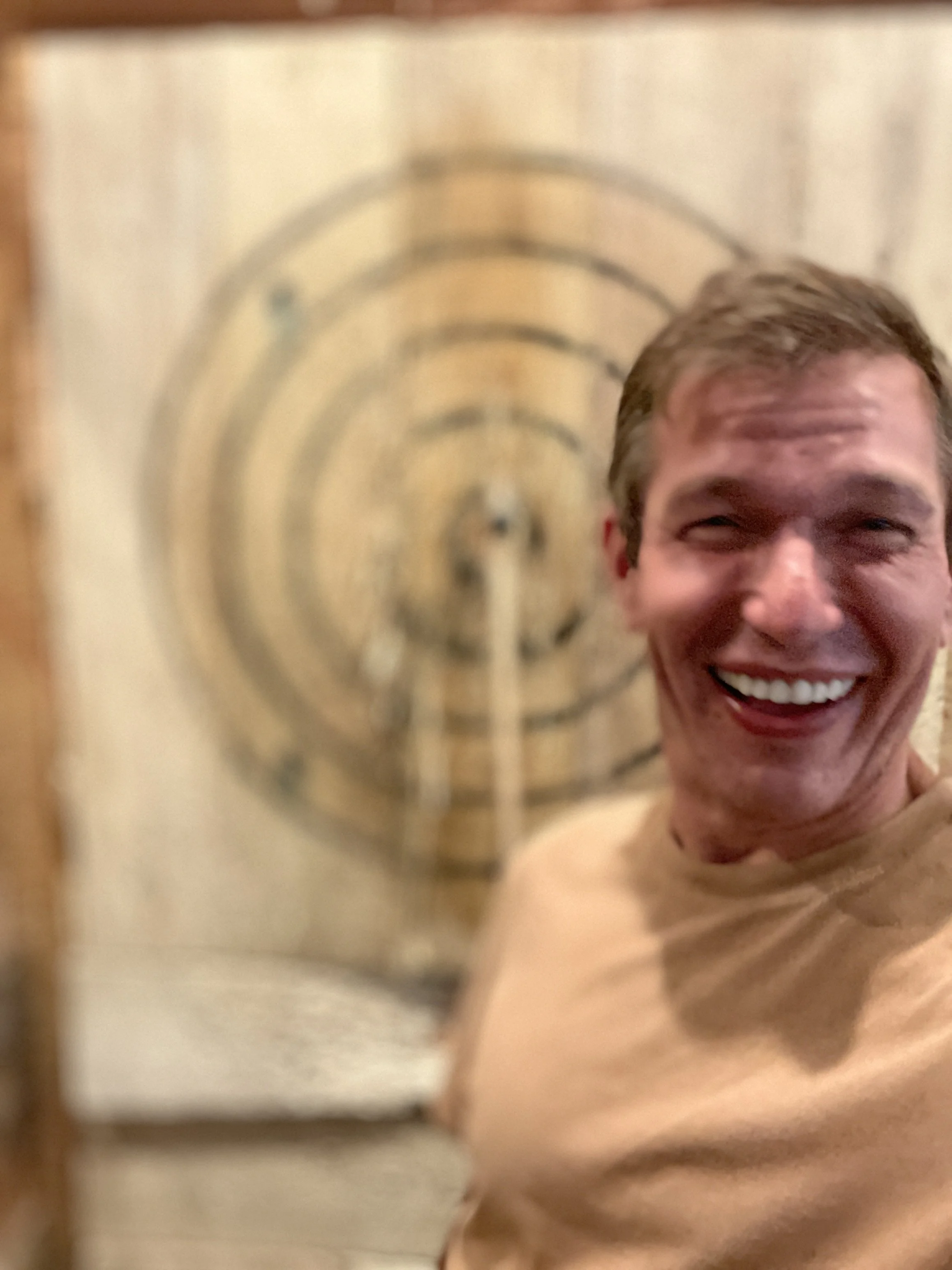 A man smiling broadly, showing his teeth, with a bullseye target in the background.
