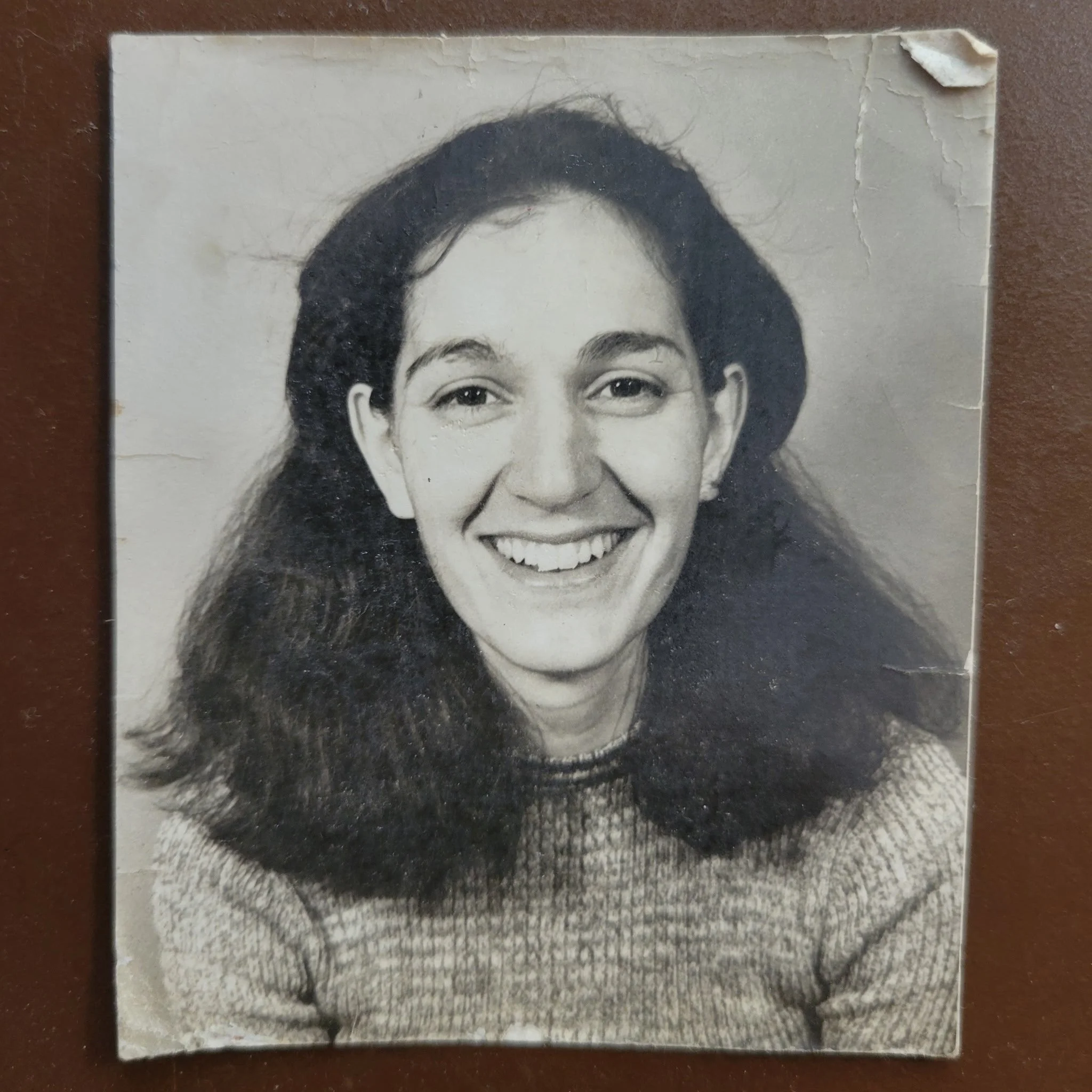 Black and white photo of a smiling woman with long dark hair, wearing a sweater, with some tear and corner damage.