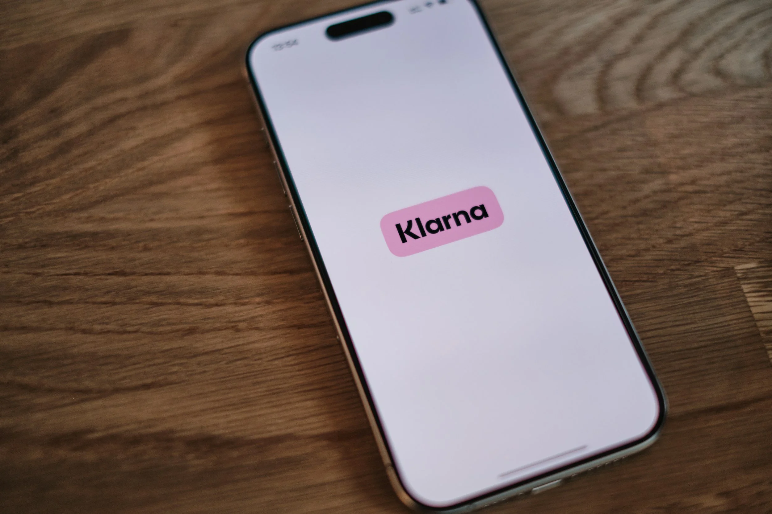 Smartphone med Klarna-appens logotyp på skärmen, vilande på en träyta.