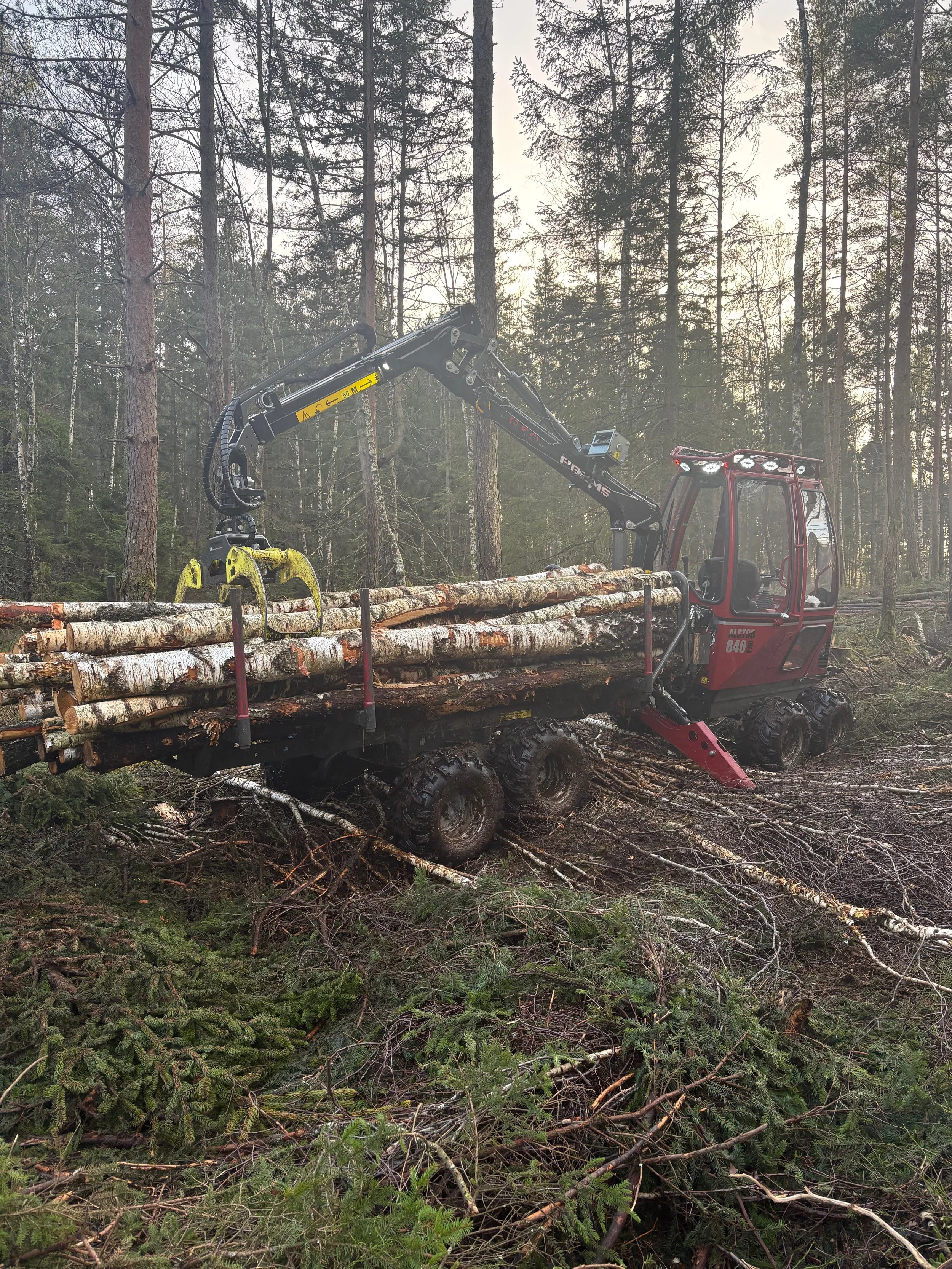 En hydraulisk kran på ett flerhjuligt fordon som skördar stockar i en skog.