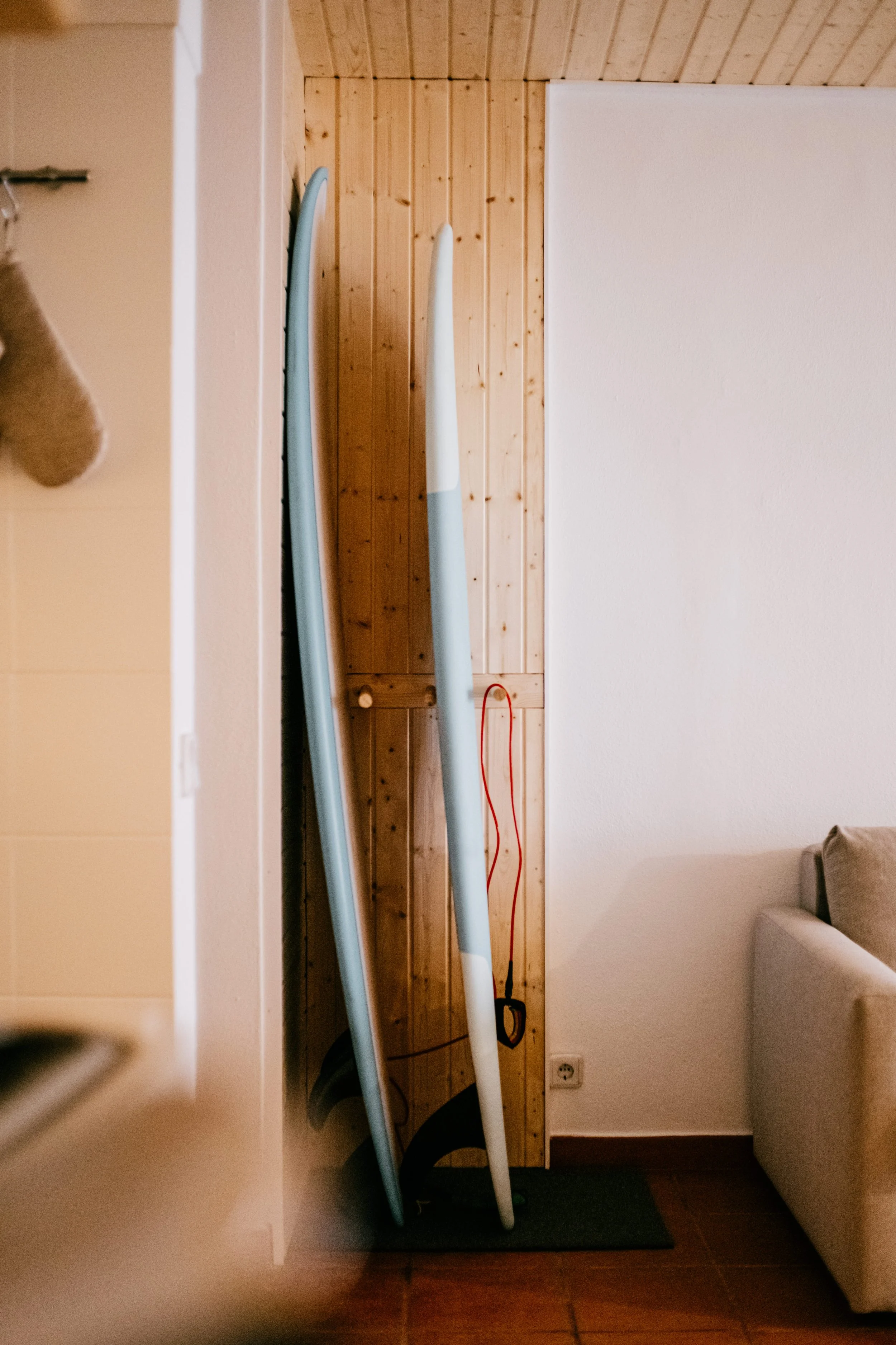 Two surfboards leaning against a wooden wall in a room with beige walls and a sofa.
