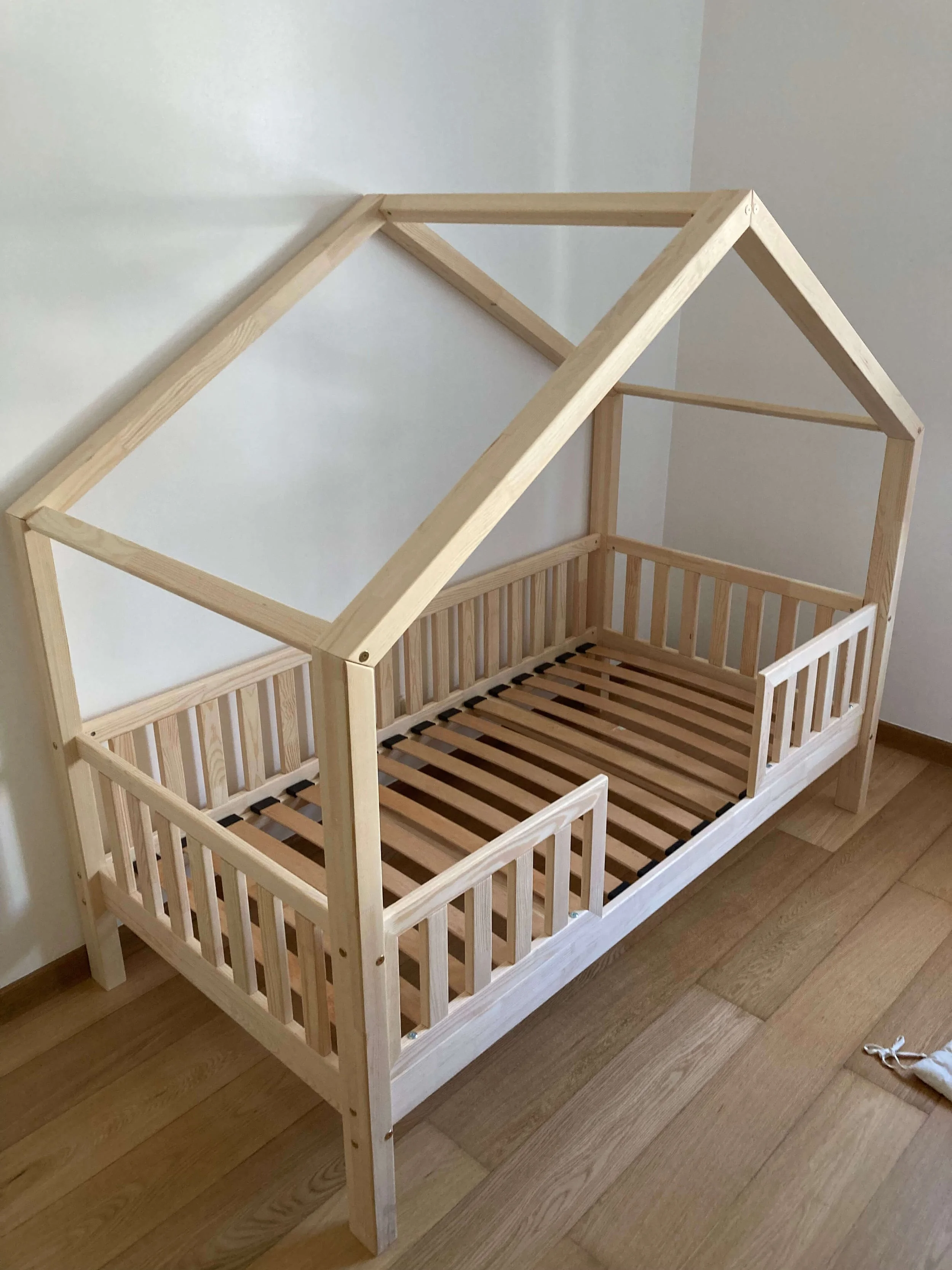 Wooden bed frame designed for a child's house-shaped bed with a slanted roof.