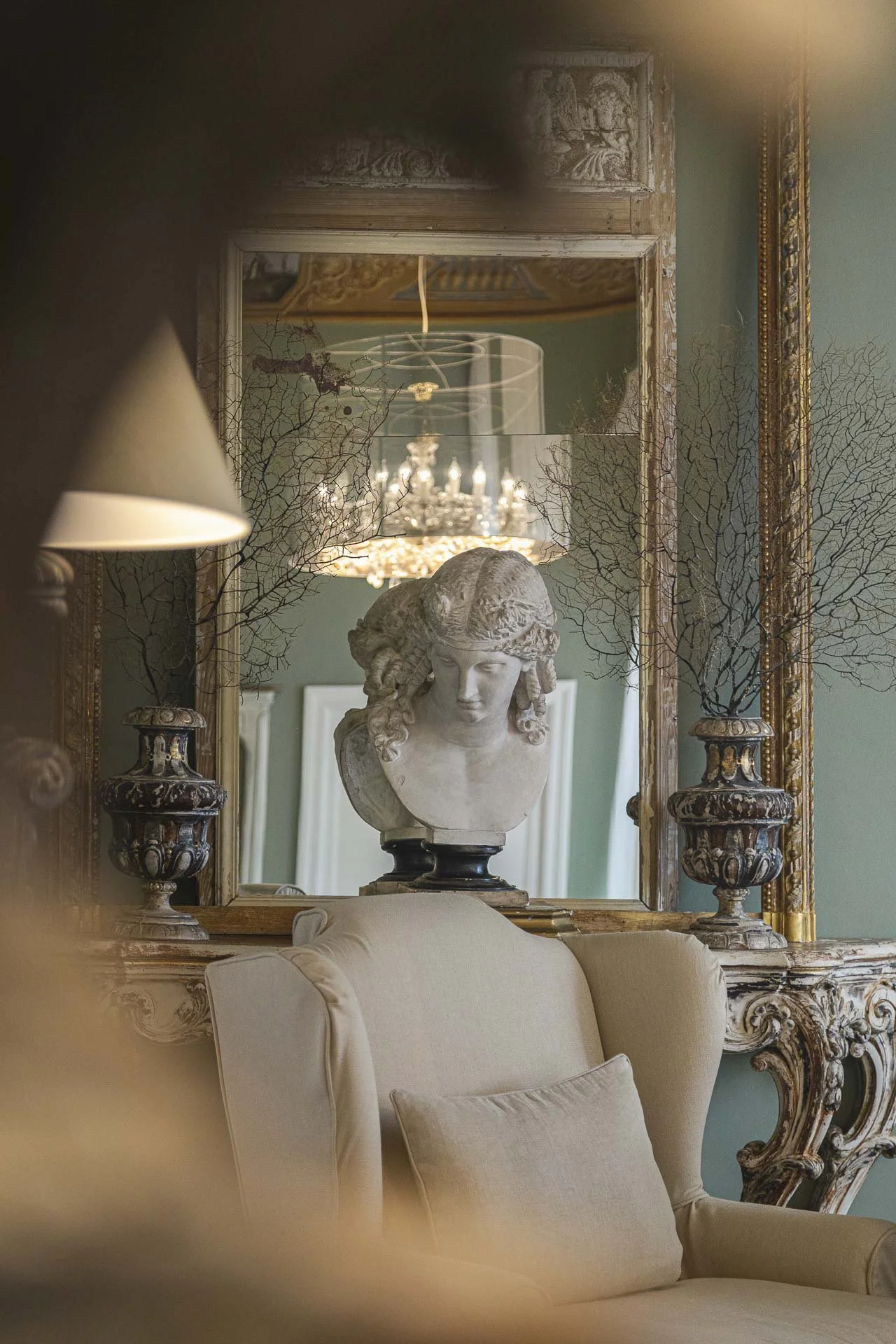 Elegant vintage interior with a marble bust sculpture of a woman, ornate gold-framed mirror, and classic decor elements.