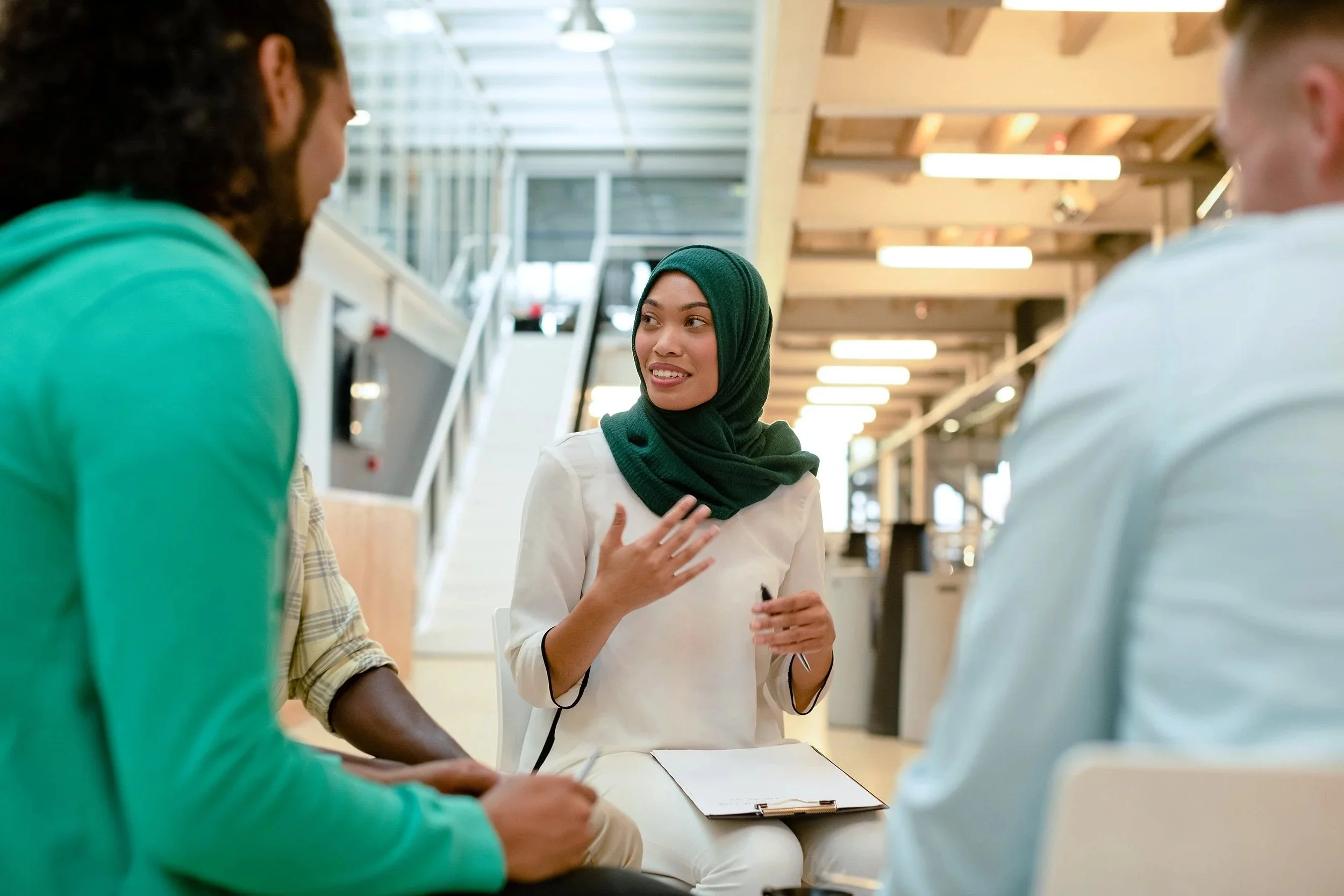 Three professionals engaged in a small group discussion in a modern office, with a woman gesturing as she speaks
