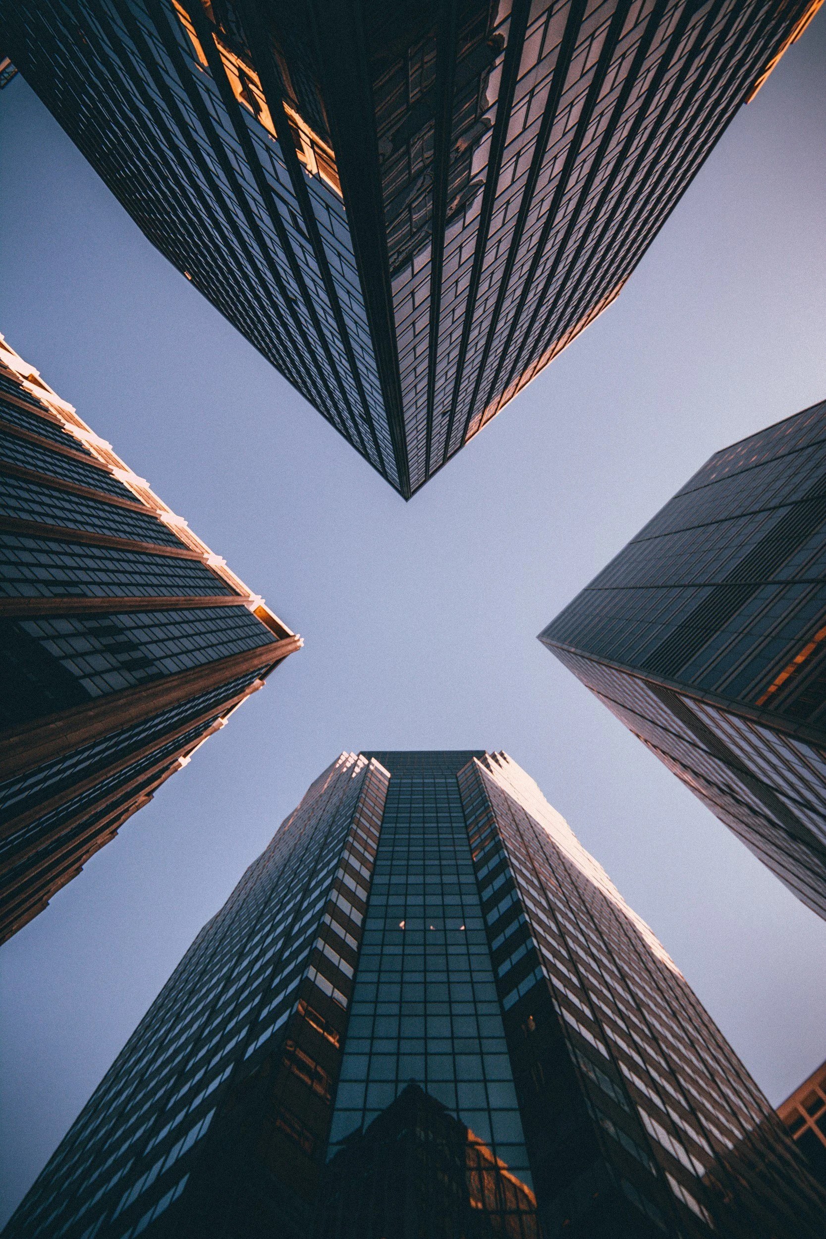 Looking up at four skyscrapers with glass facades against a clear blue sky.