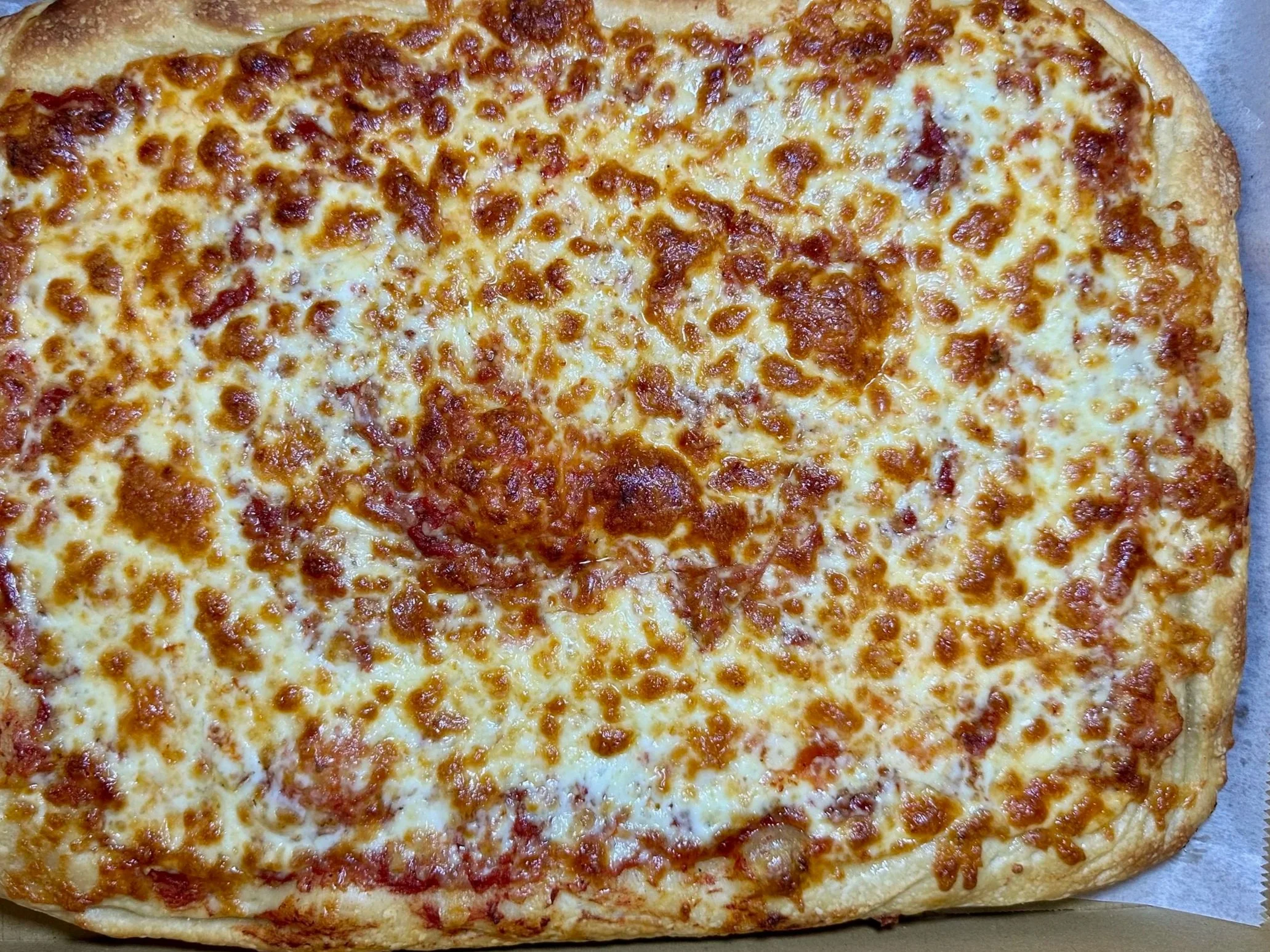 A large rectangular cheese pizza in a cardboard box with cheese topping and a golden brown crust.