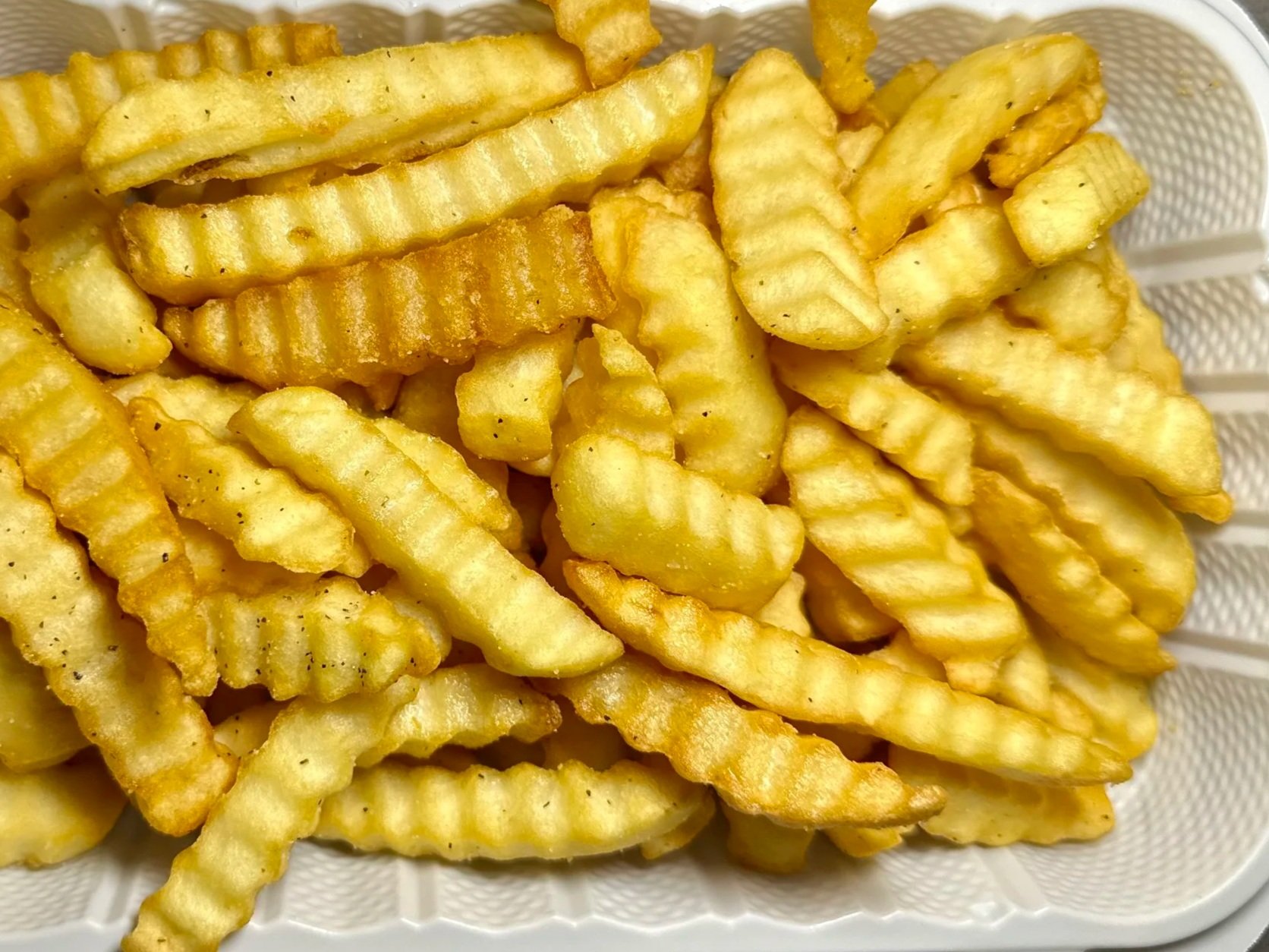 A white container filled with crinkle-cut French fries on a gray surface.