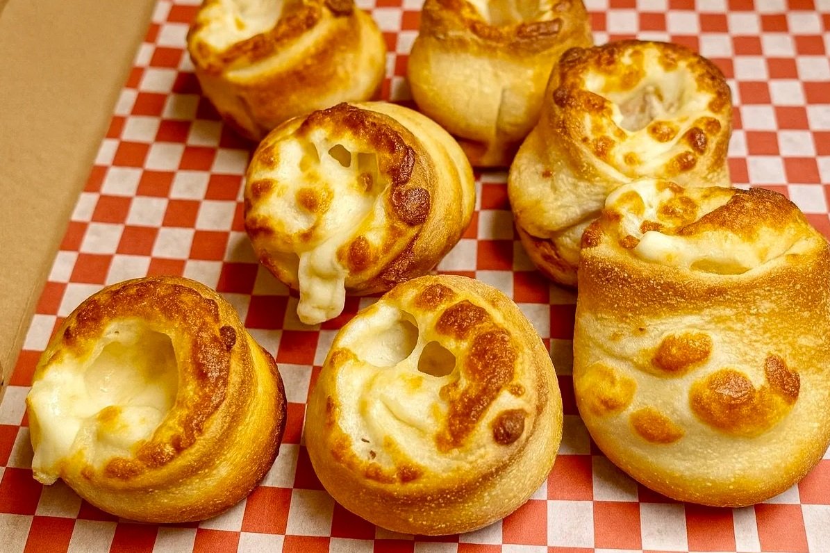 Seven cheesy bread rolls in a cardboard box with red and white checkered paper lining.