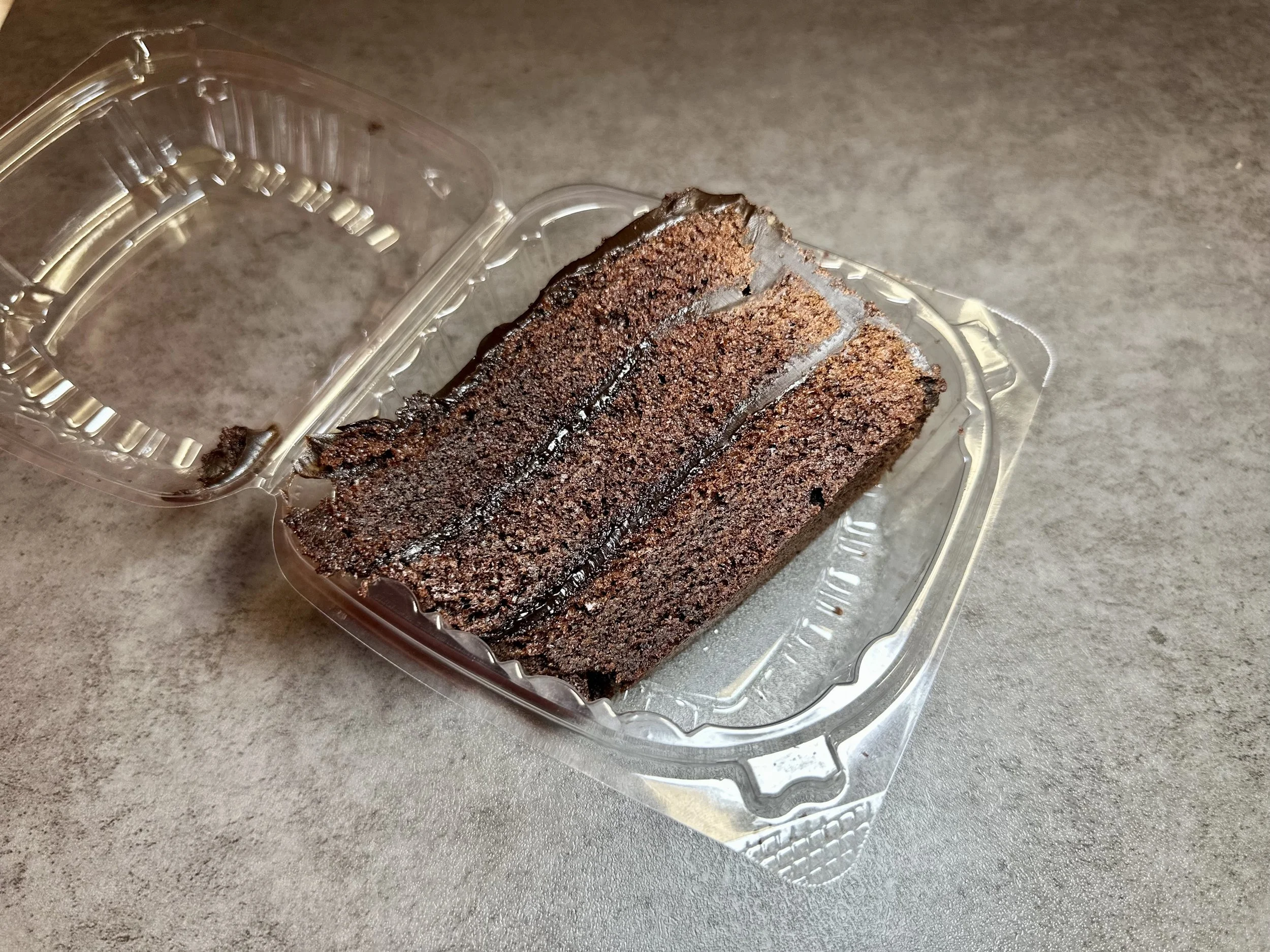 Chocolate cake slices in a clear plastic container on a gray surface.