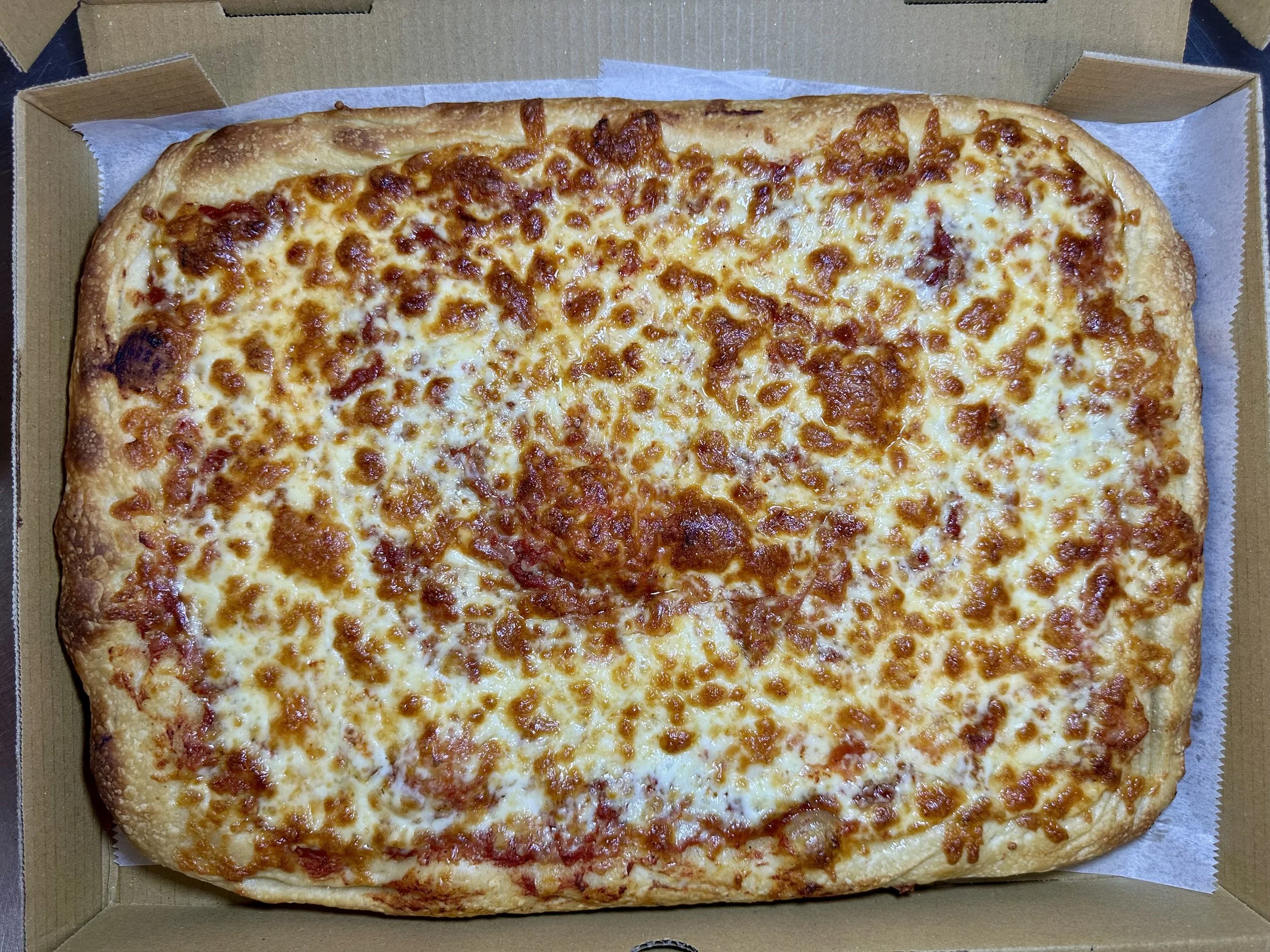 A large rectangular cheese pizza in a cardboard box, topped with melted cheese and a crispy crust.