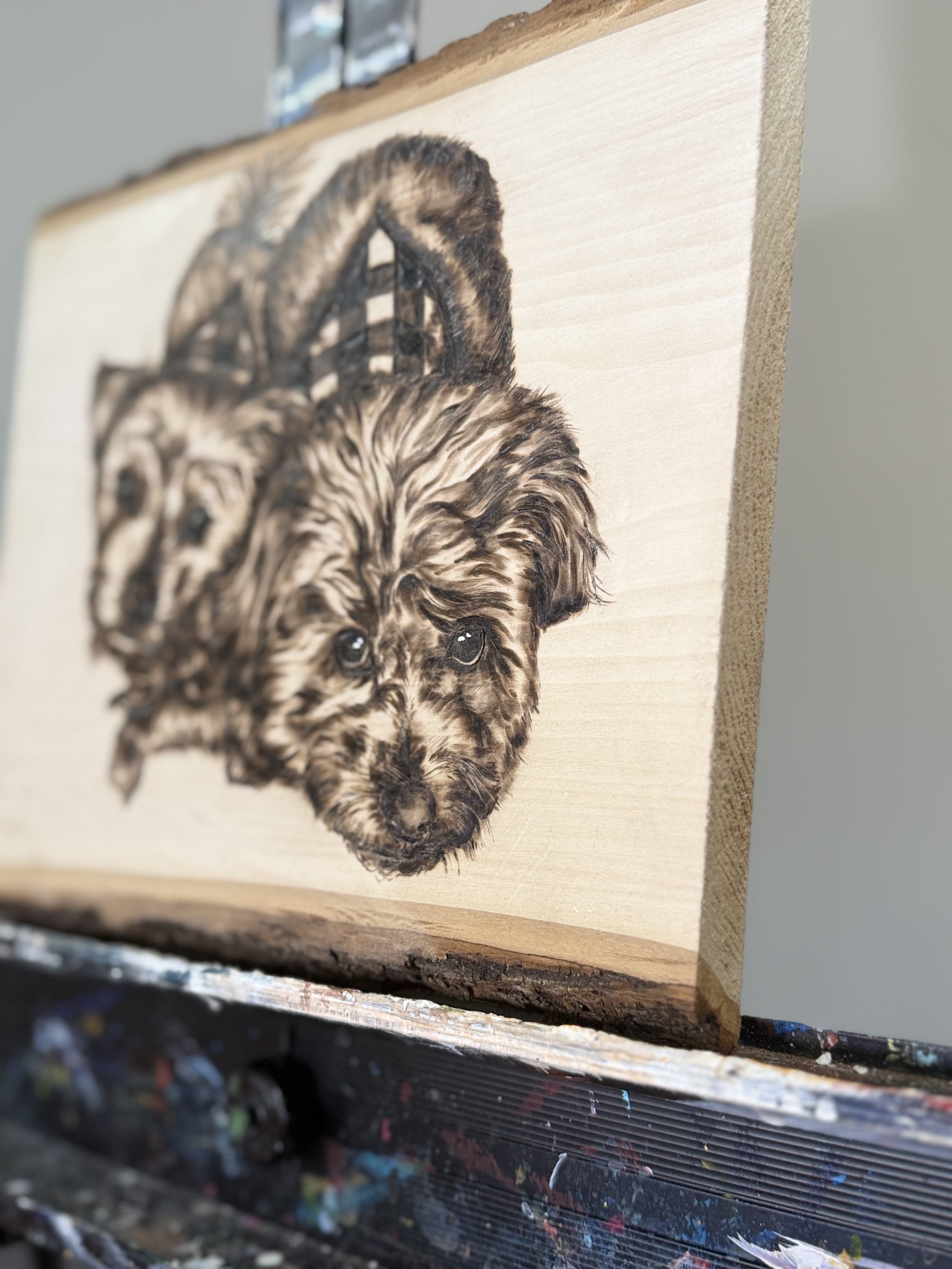 A wooden canvas with a detailed black and white portrait of a fluffy puppy with expressive eyes.