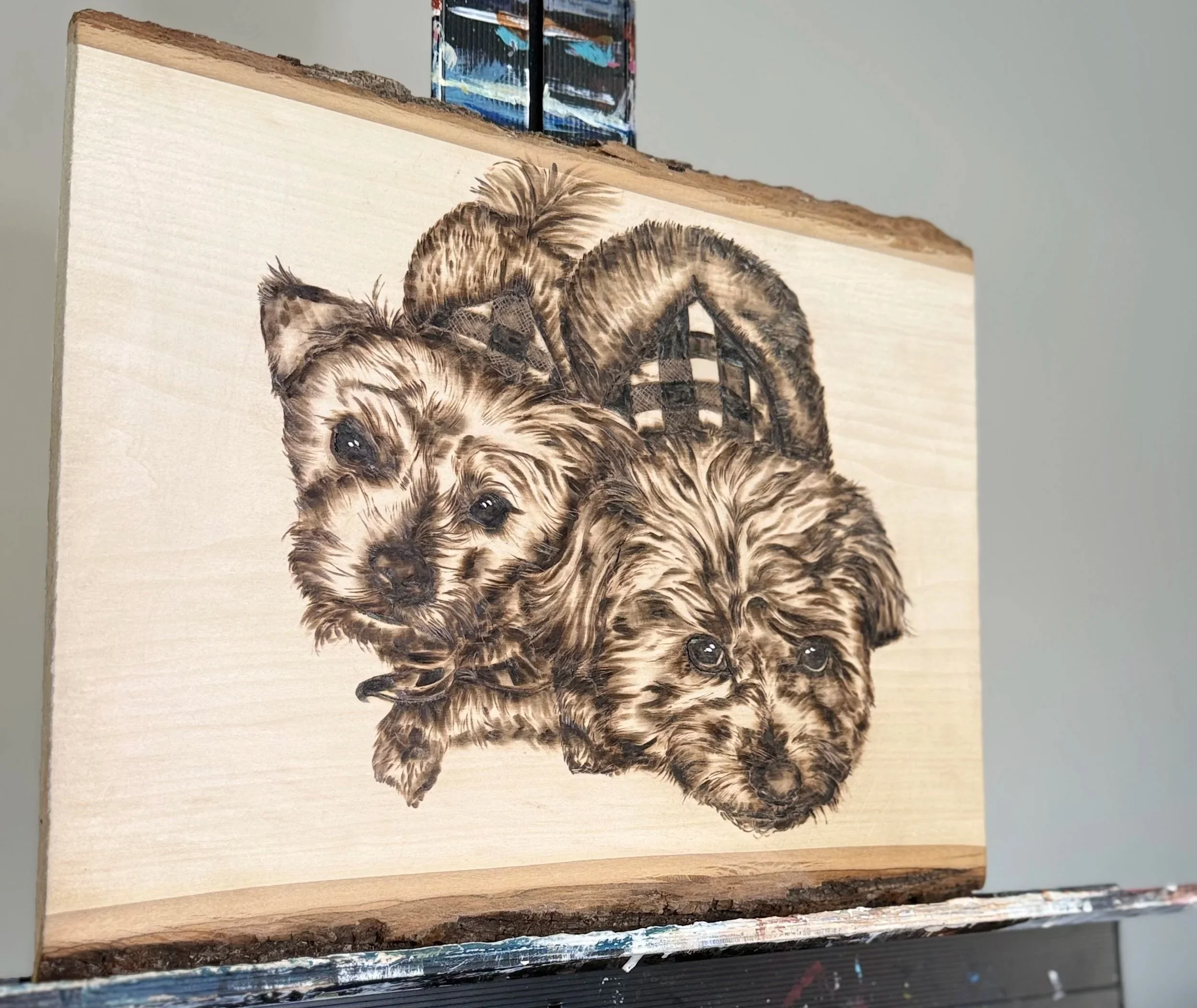 Wooden plaque with detailed painting of two puppies, one with a bow, on a light wood background.