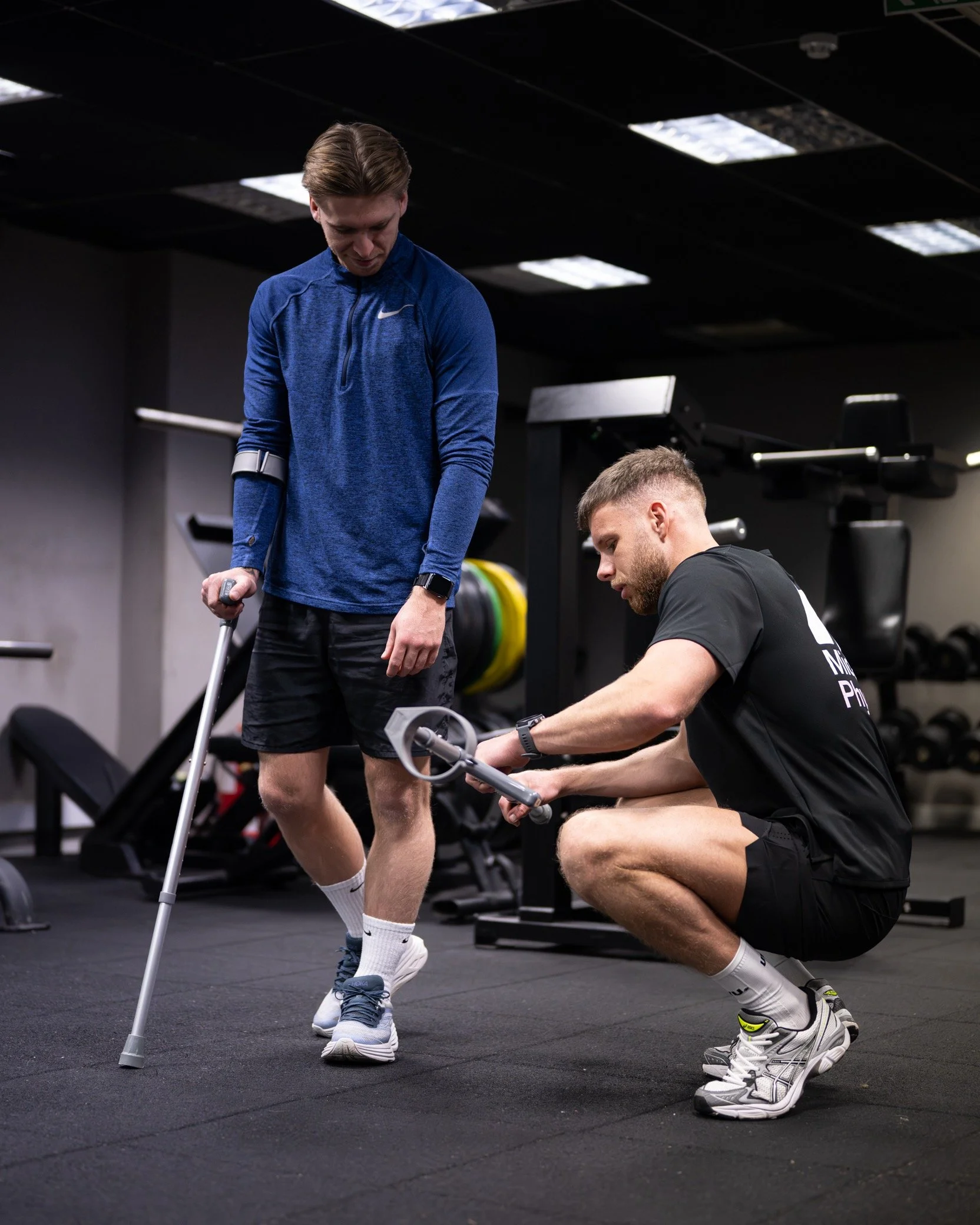 A man with crutches training with a trainer at the gym.