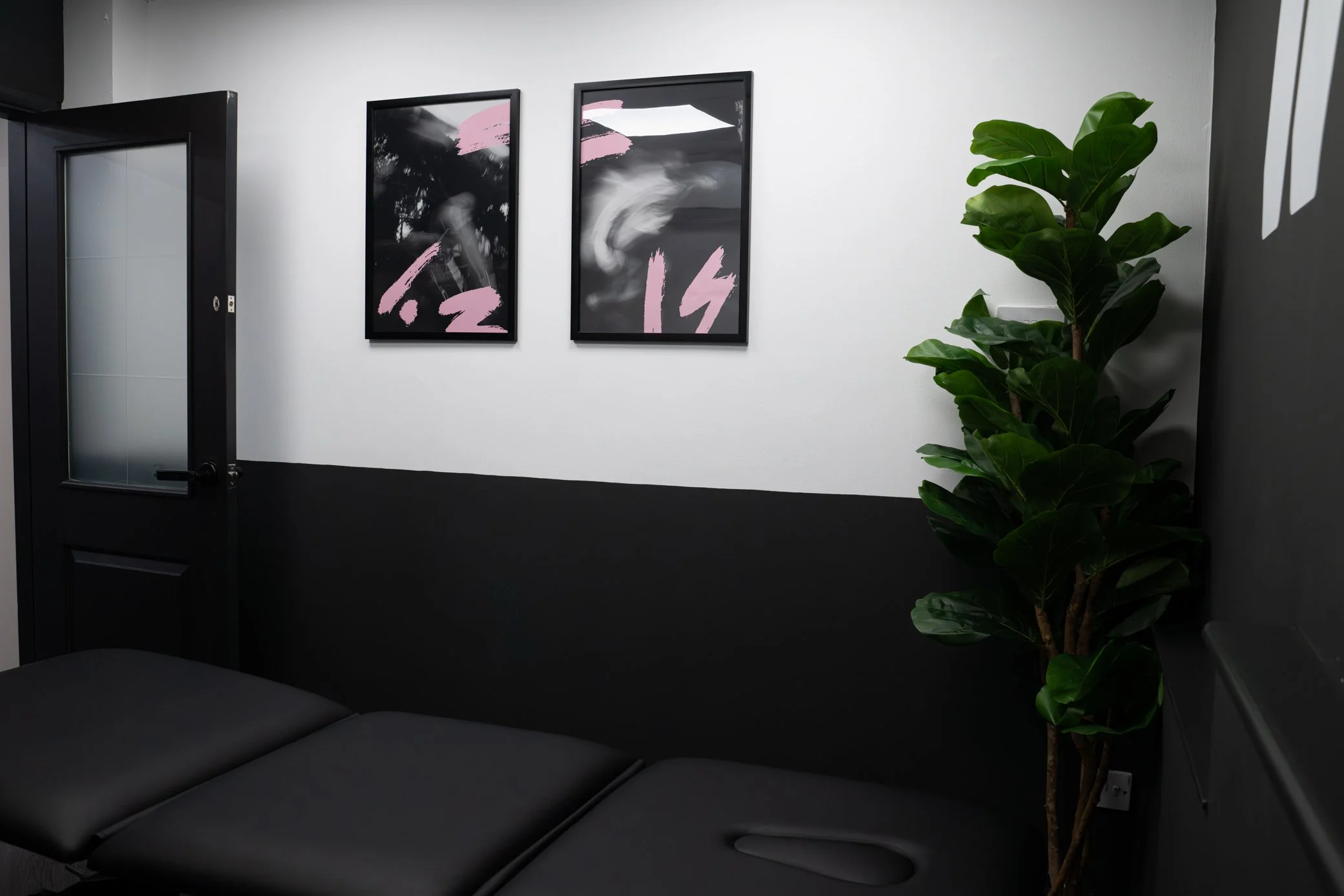 Waiting room with black and white wall art, black door, black leather chair, and green potted plant.