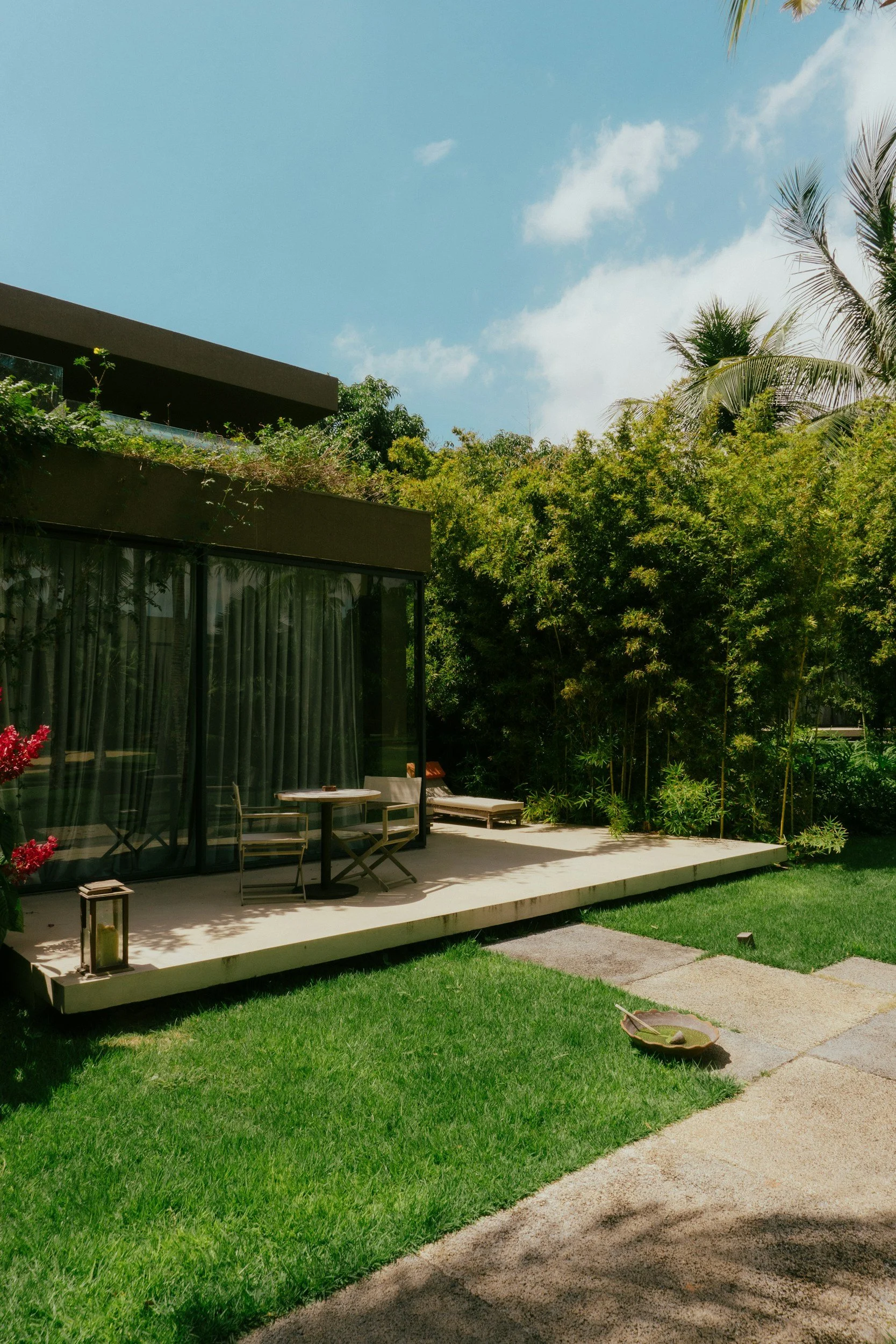 Modern house patio with outdoor table and chairs, surrounded by green lawn and lush trees under blue sky. Anita McGovern Real Estate