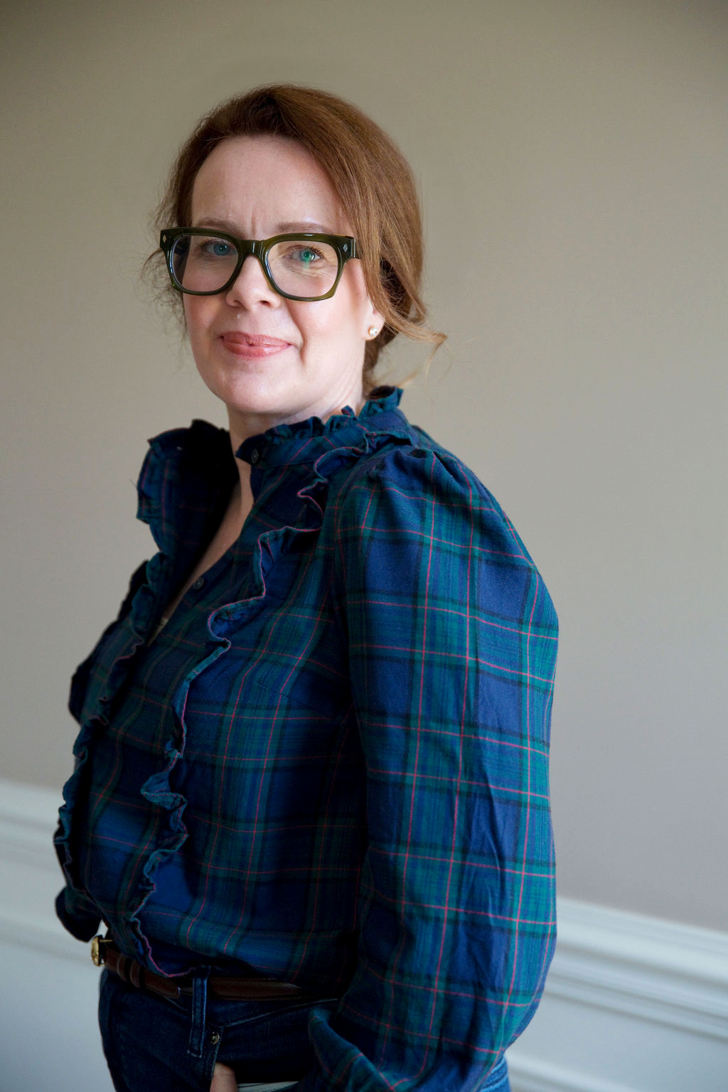 A woman with red hair, wearing glasses, a plaid shirt with ruffled detail, and standing against a plain background. Anita McGovern Real Estate